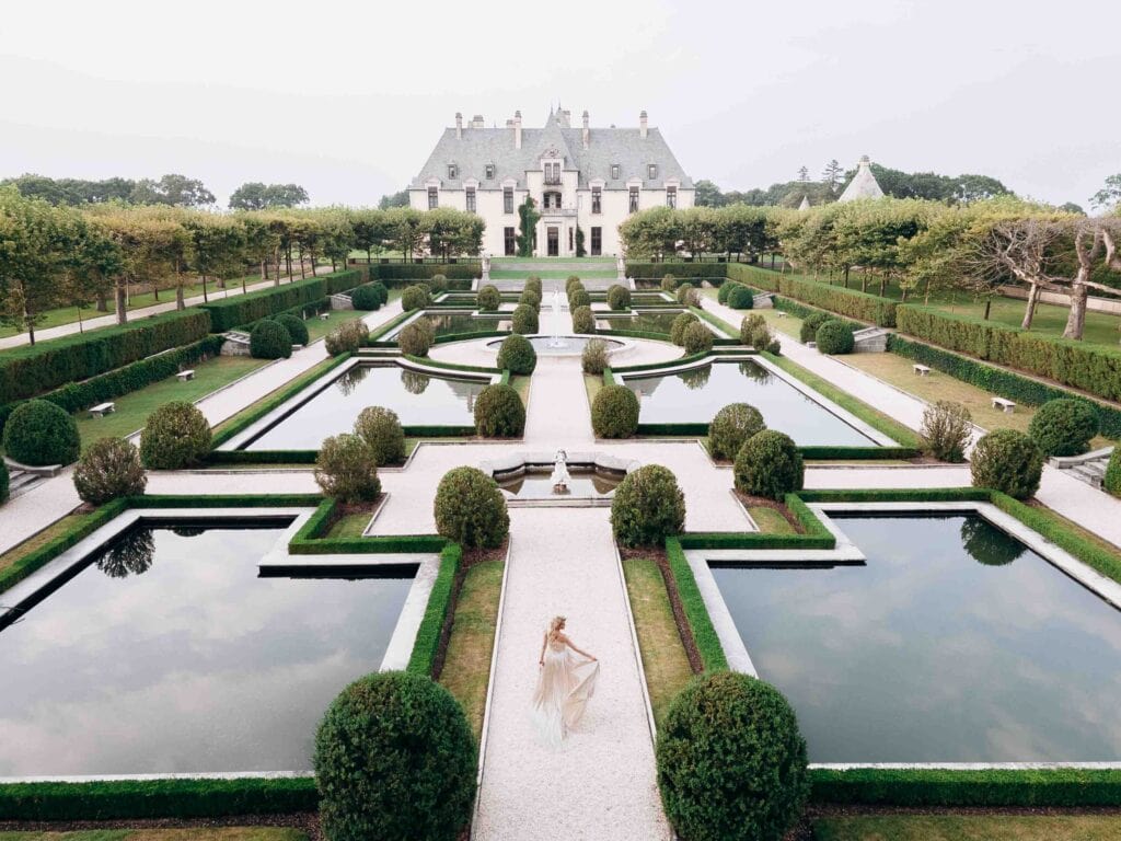 Aerial view of a symmetrical garden with trimmed hedges, water features, and a central pathway leading to a large historic estate in New York, NY.
