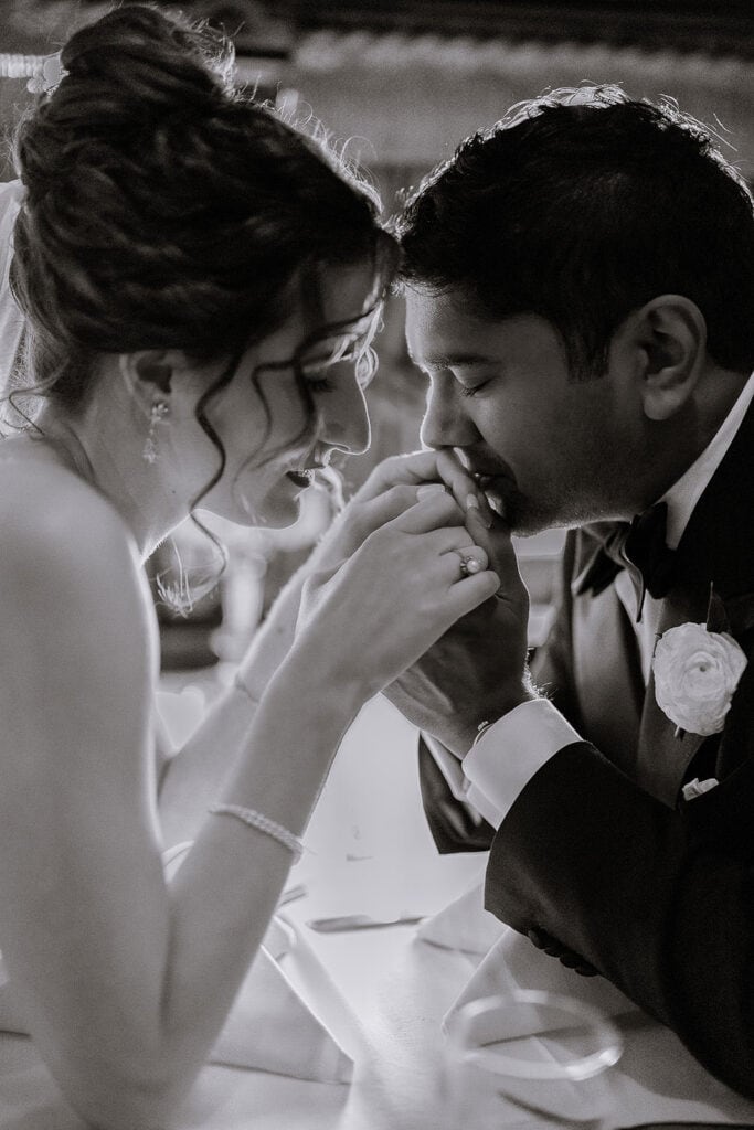 Black and white close-up of a groom tenderly kissing the bride's hand, both with eyes closed, showcasing intimate connection and elegant wedding attire at The Madison Hotel Morristown, NJ.
