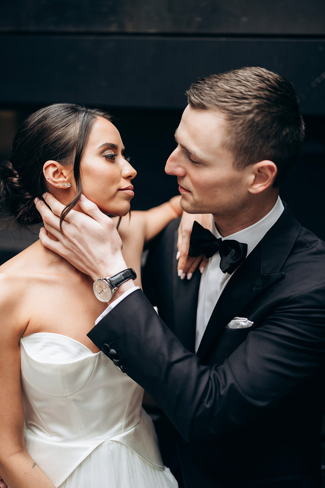 Close-up of a couple in elegant evening wear, the groom in a black tuxedo holding the bride's neck as they gaze at each other in New York, NY.