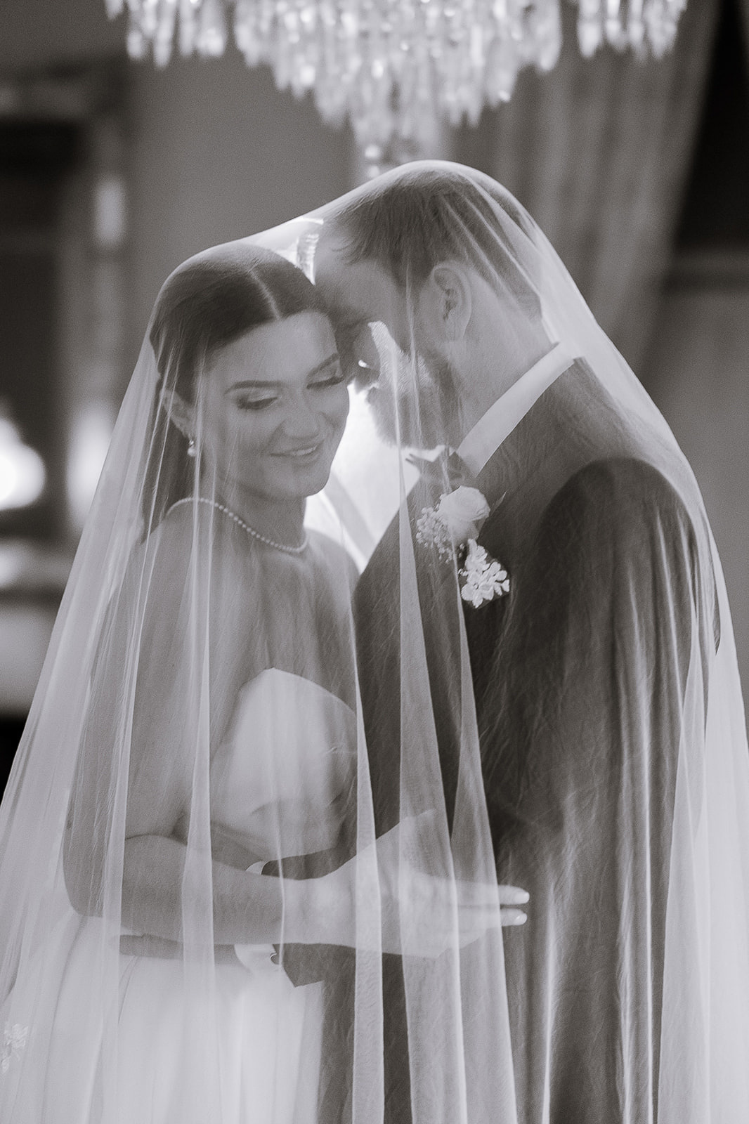Bride and groom embracing closely under a sheer veil with soft chandelier light in a Manhattan wedding venue.