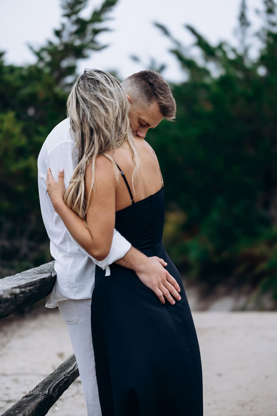 Couple embracing near rustic wooden fence with green foliage in the background at Barnegat Light, NJ.