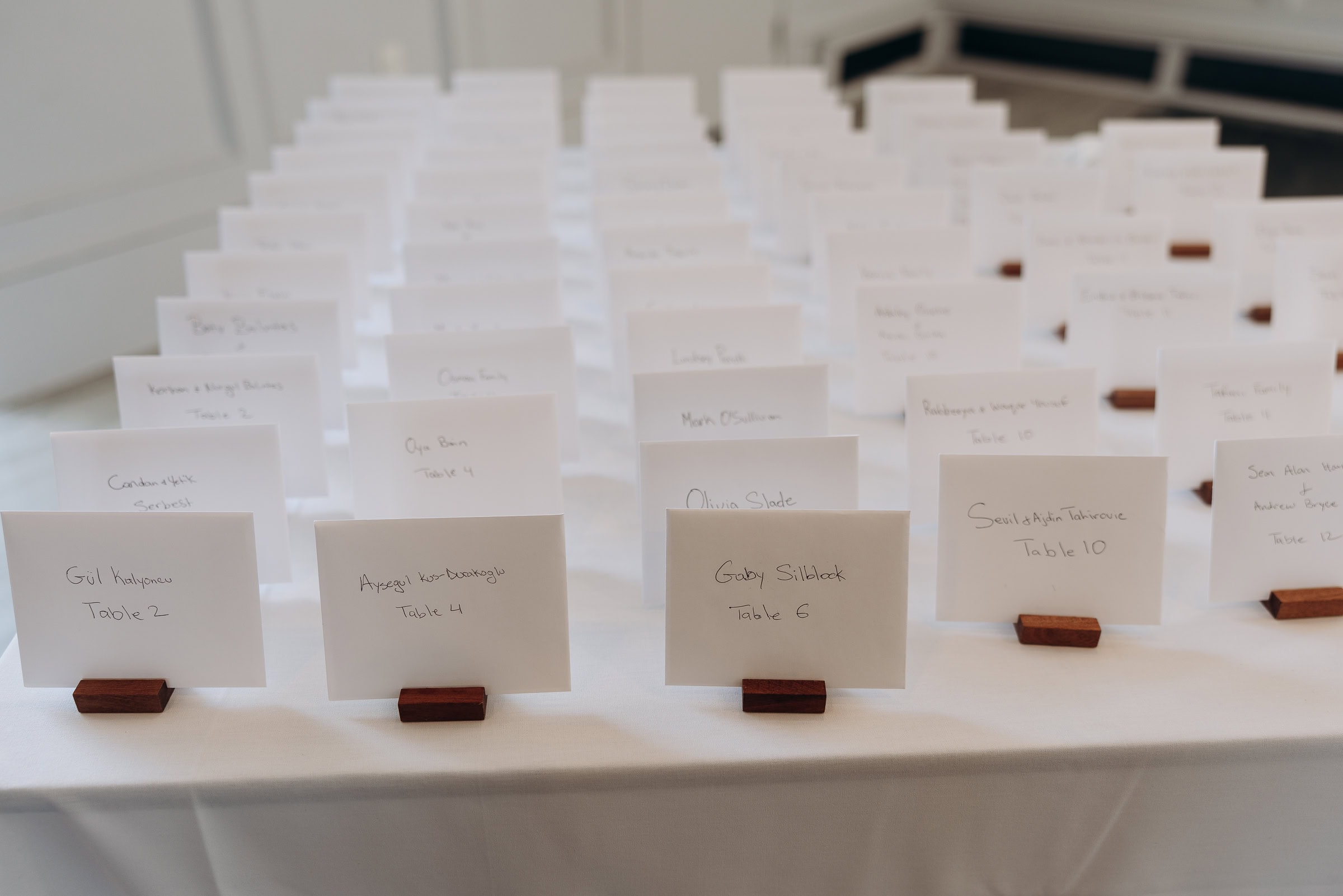 Rows of white handwritten escort cards on wooden holders arranged on a white tablecloth at Hudson House, Jersey City, NJ.
