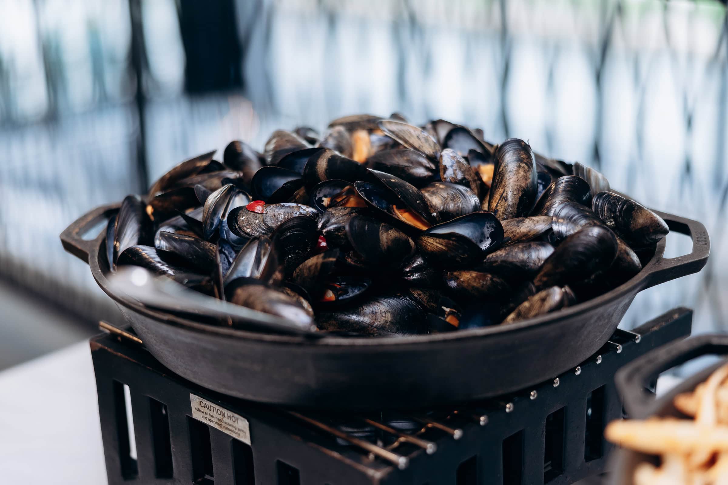 Close-up of steamed mussels with dark shells in a cast iron pan, blurred background with natural light, Hudson House Jersey City NJ.