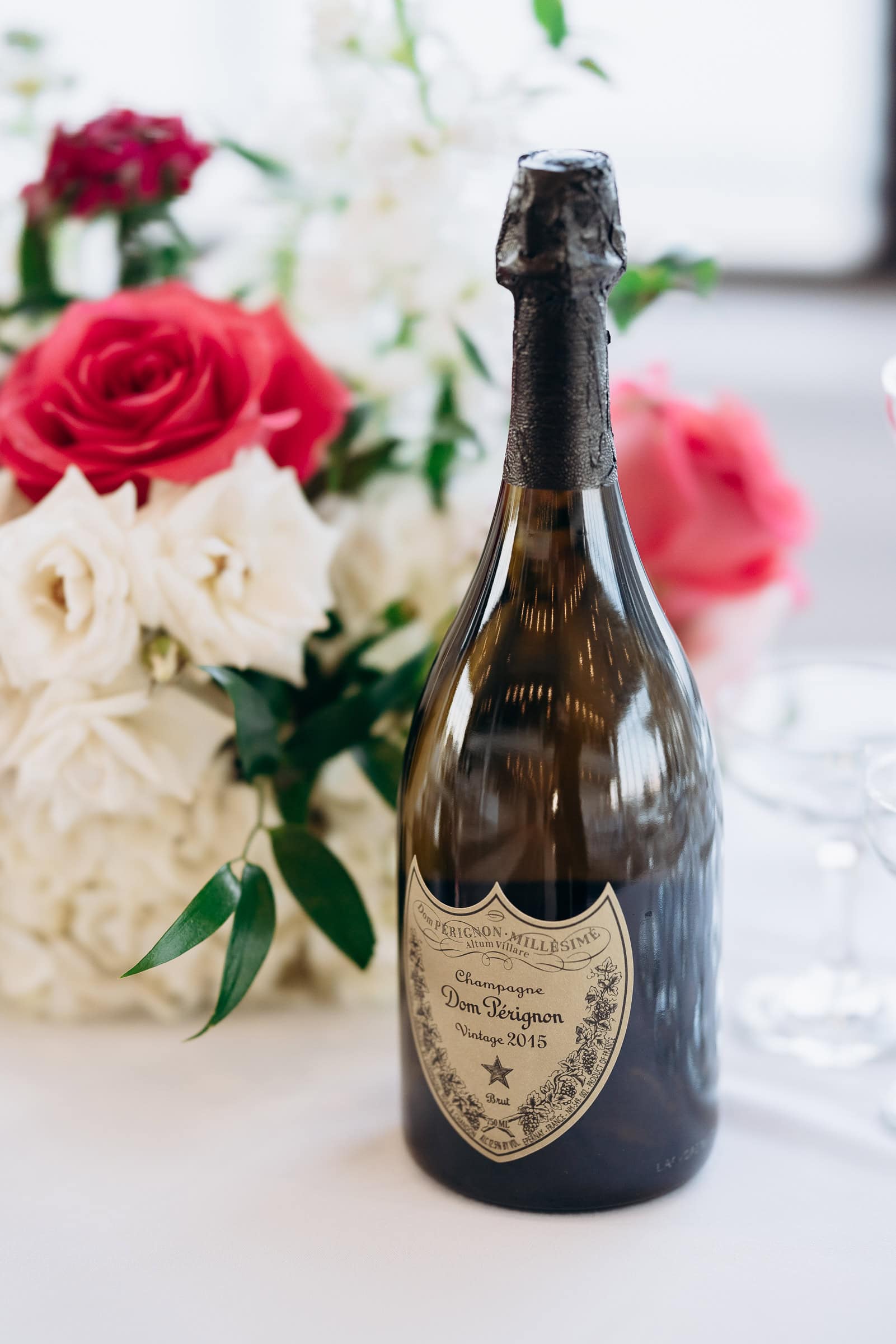 Close-up of a Dom Pérignon 2015 champagne bottle with blurred white and pink roses in the background on a white tablecloth at Hudson House, Jersey City.