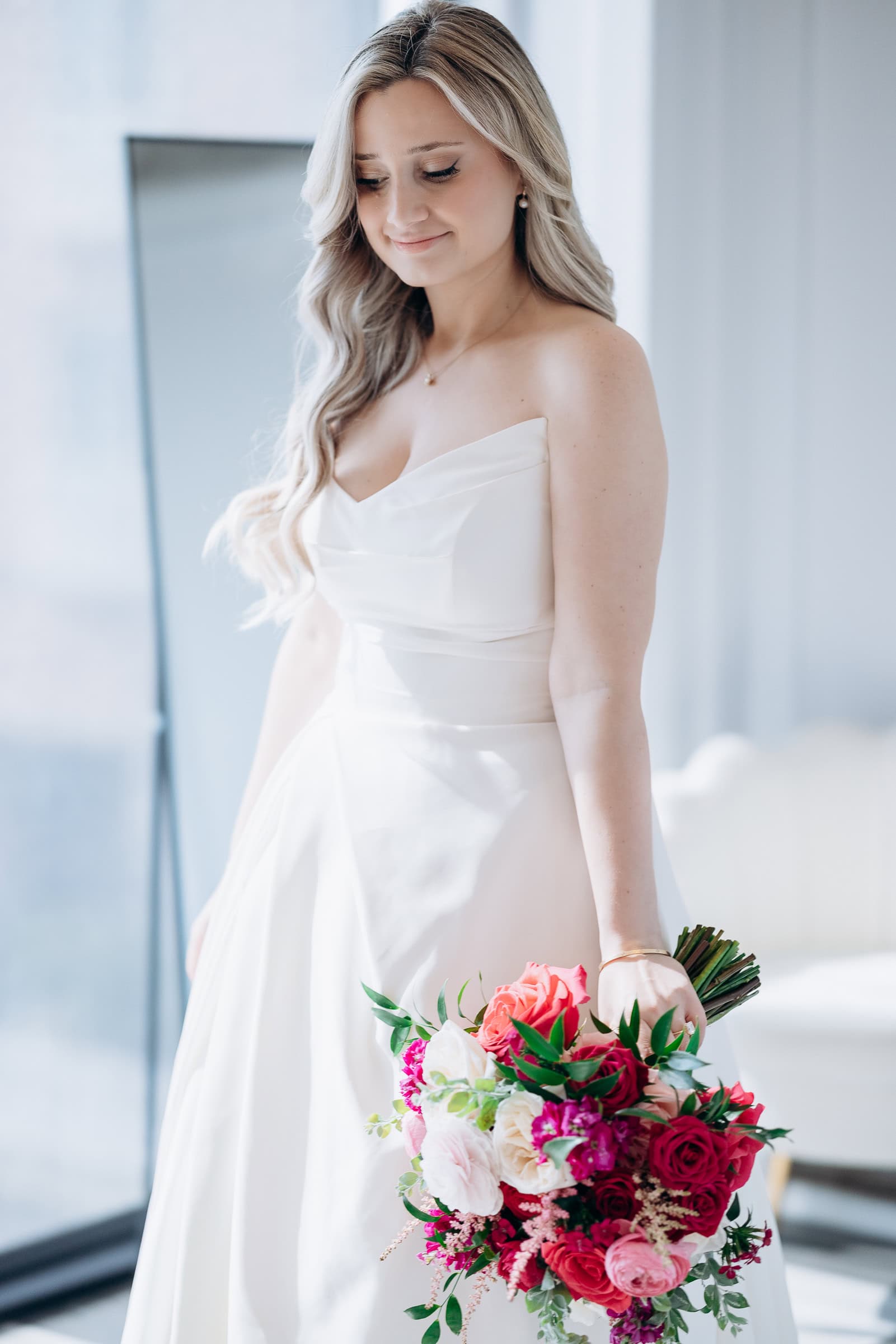 Bride in satin strapless wedding dress holding vibrant pink and white bouquet indoors at Hudson House, Jersey City, NJ.