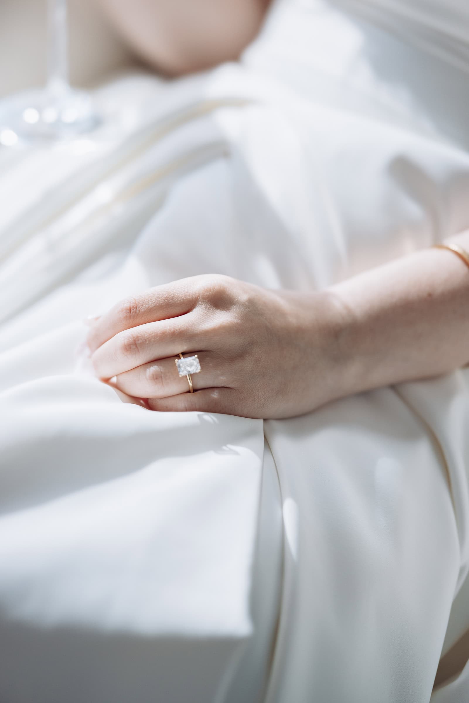 Close-up of hand wearing emerald-cut diamond ring on white fabric with soft natural light, Hudson House, Jersey City, NJ.
