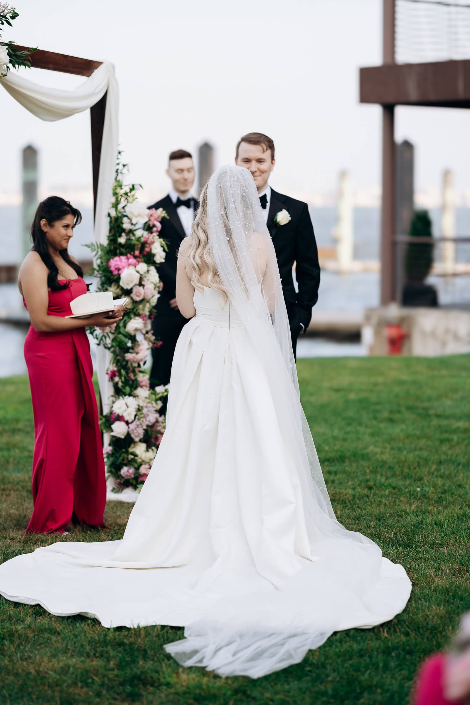 Bride in pearl-embellished veil and white gown facing groom in black tuxedo during outdoor wedding ceremony at Hudson House, Jersey City, NJ