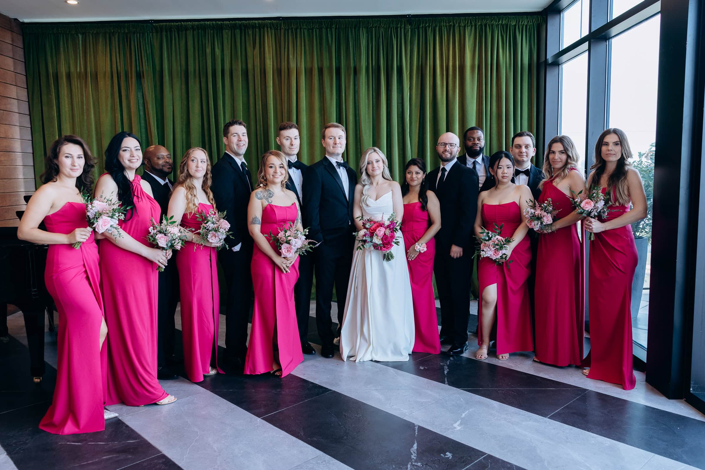 Bridal party with bride in white gown, bridesmaids in fuchsia dresses holding pink bouquets, and groomsmen in black tuxedos at Hudson House, NJ.