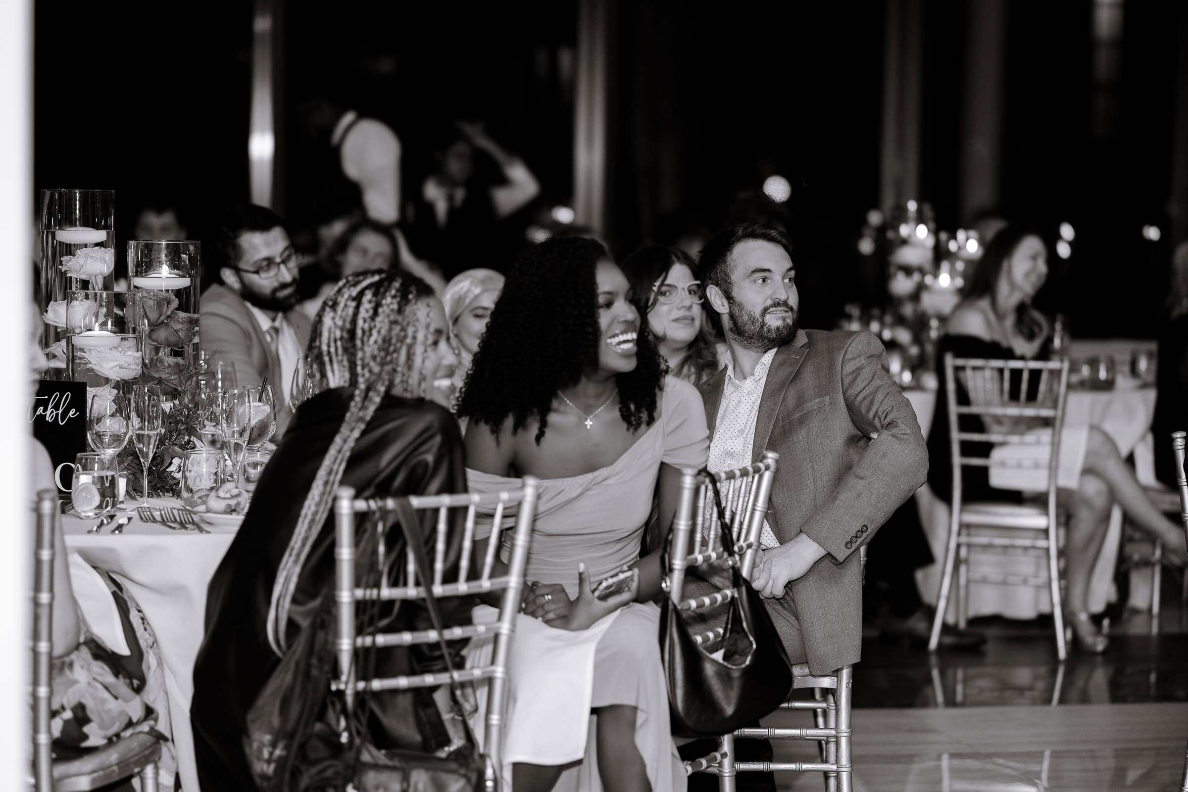 Group of guests seated at a candlelit table with floral centerpieces, engaged in conversation during an evening event at Hudson House, Jersey City.