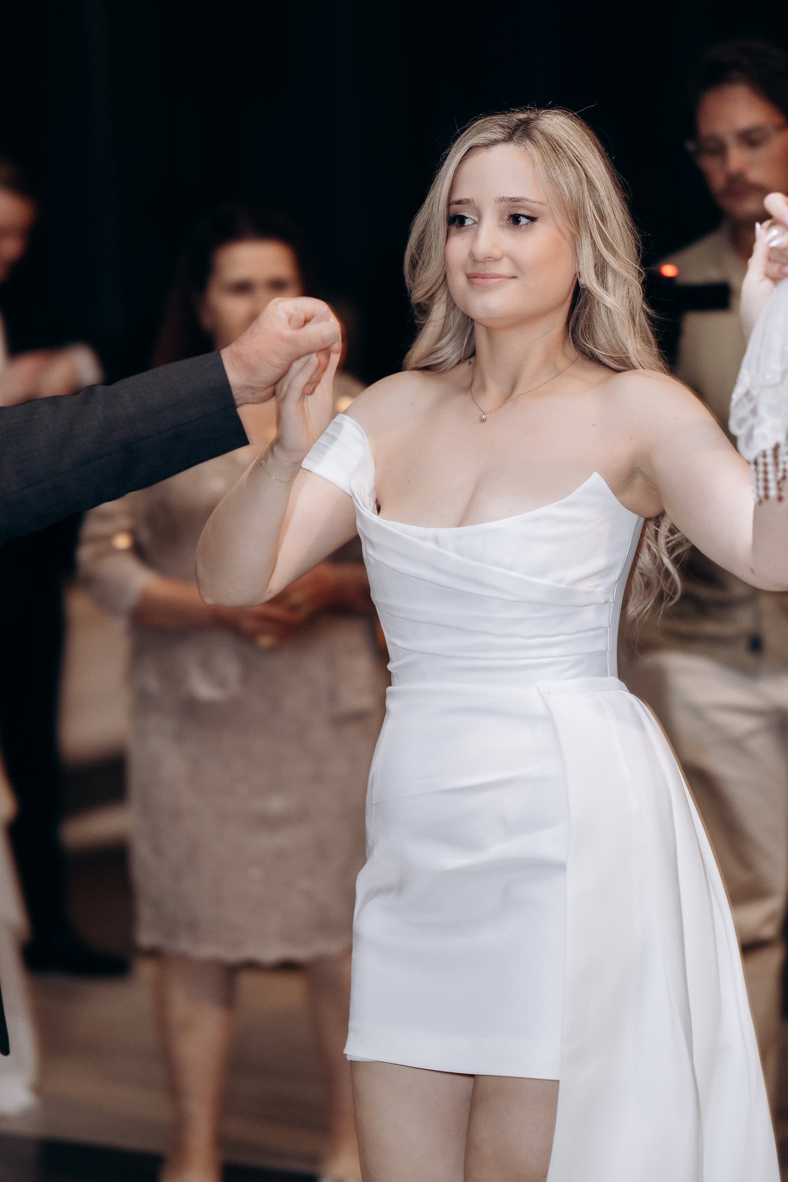 Bride in off-shoulder white satin dress holding hands with a partner during a wedding celebration at Hudson House, Jersey City, NJ.