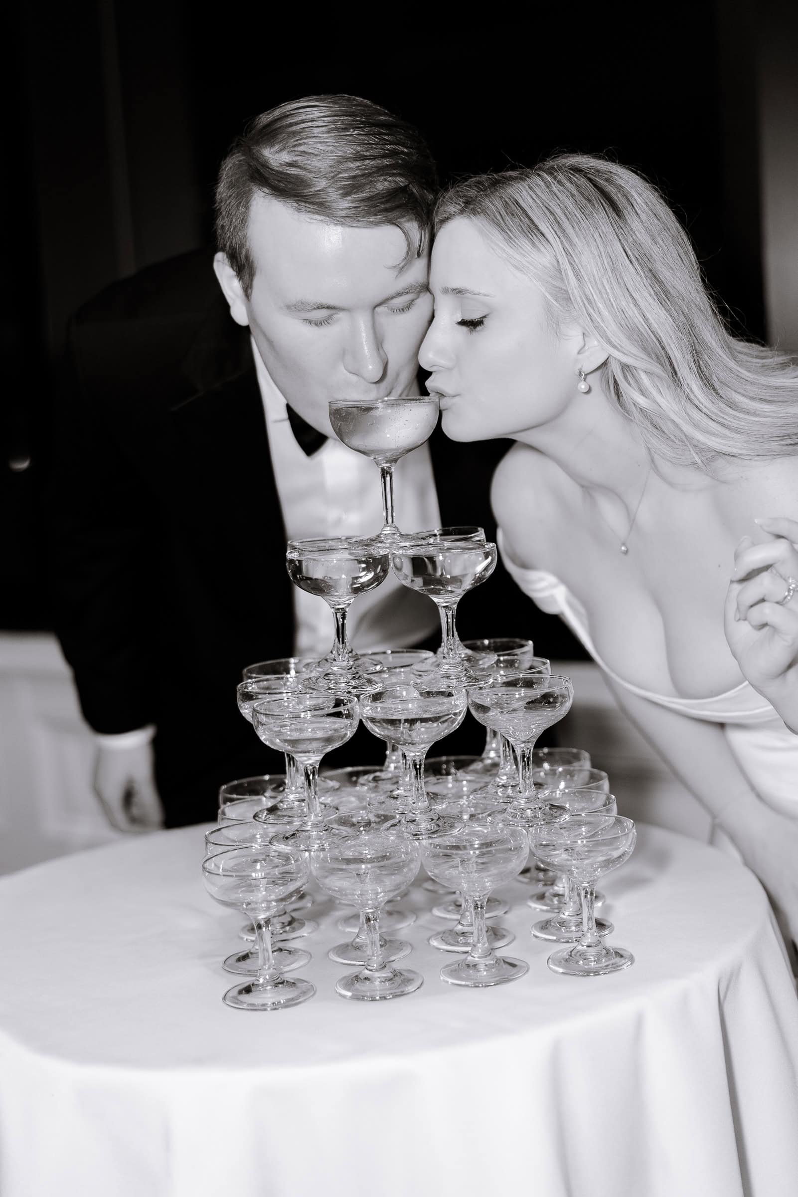 Couple in formal attire sipping champagne from the top glass of a multi-tiered champagne tower at a Hudson House wedding in Jersey City, NJ.