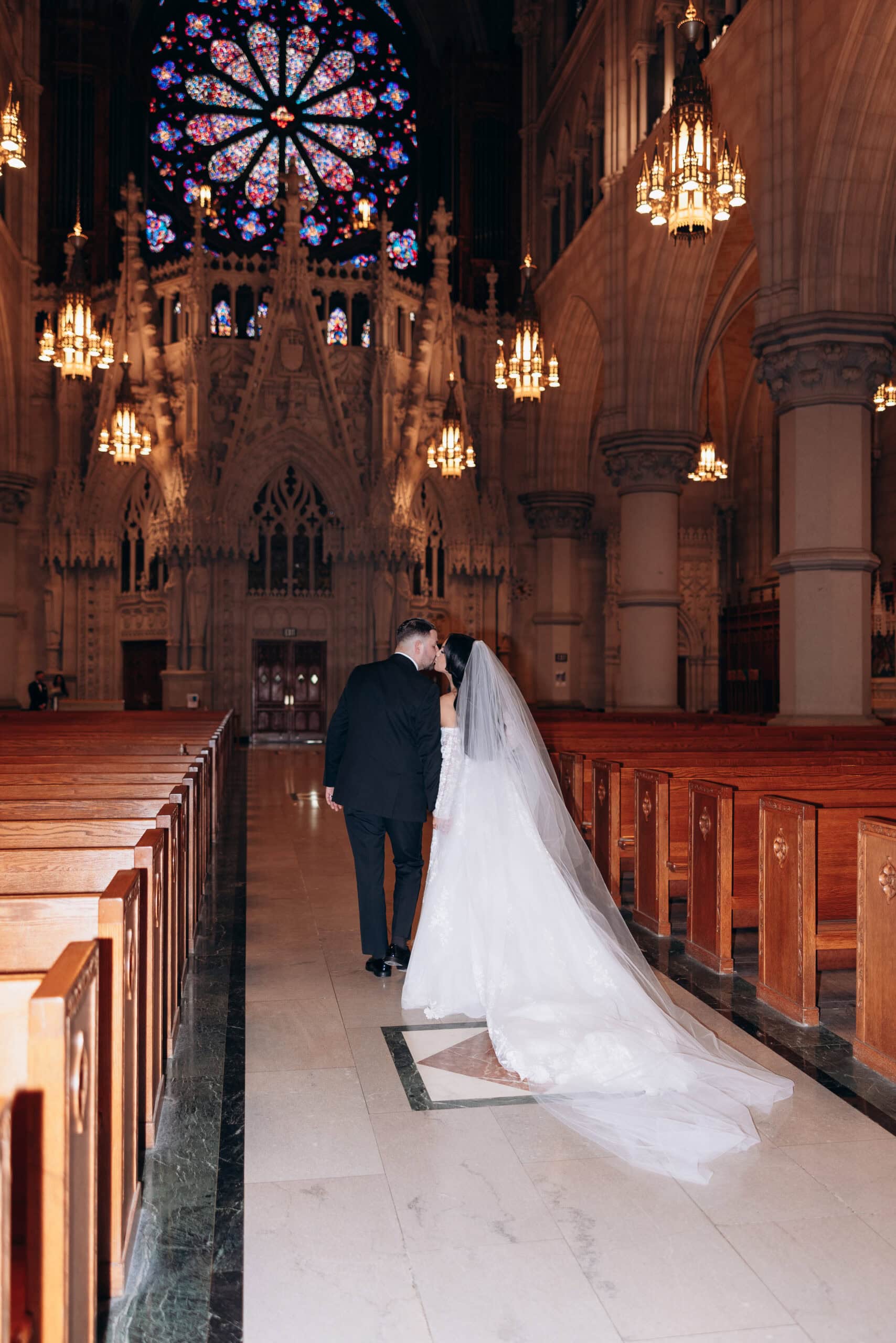 Bride and groom kissing while walking down the aisle inside The Cathedral Basilica of the Sacred Heart with stained glass rose window and ornate Gothic details overhead.