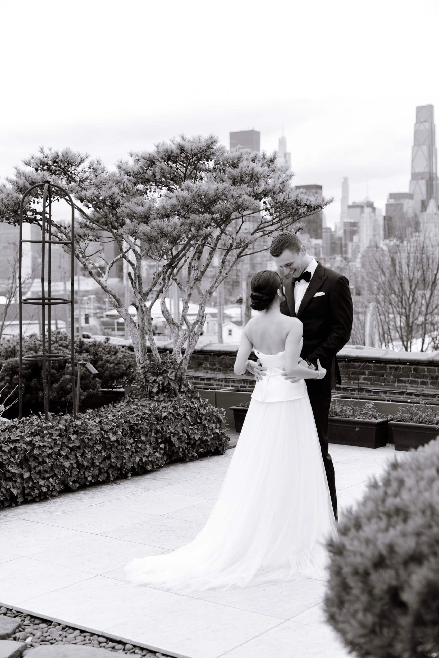 Black-and-white wedding portrait of a couple embracing on a rooftop terrace at The Foundry, with sculpted trees and the Manhattan skyline in the background.