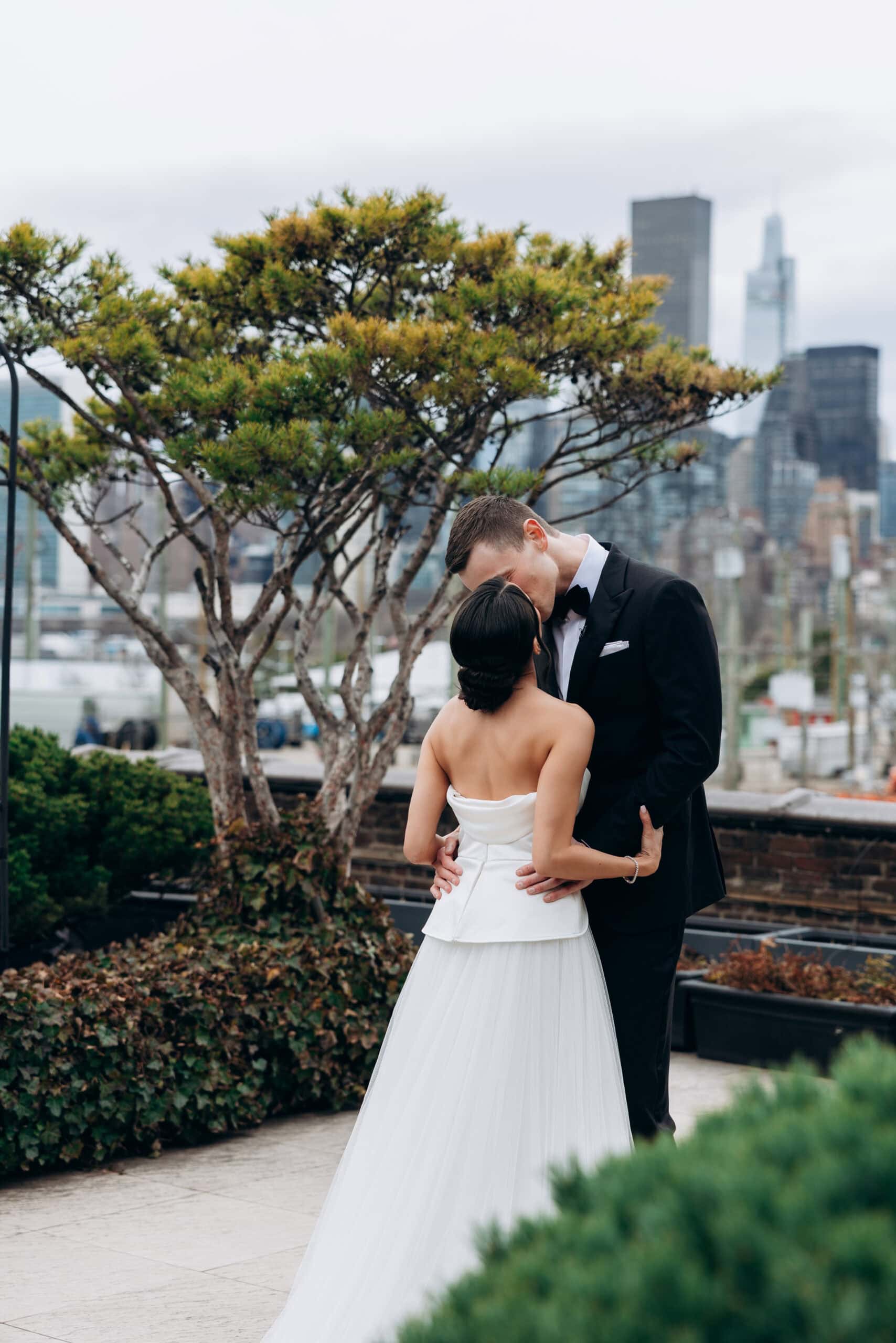 Bride and groom embracing in a rooftop garden at The Foundry with the Manhattan skyline softly blurred behind them.