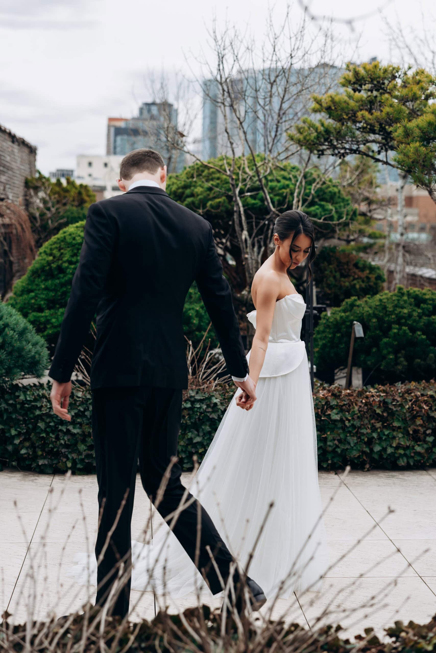 Couple holding hands and walking through the rooftop garden at The Foundry, with manicured greenery and a city skyline in the background.