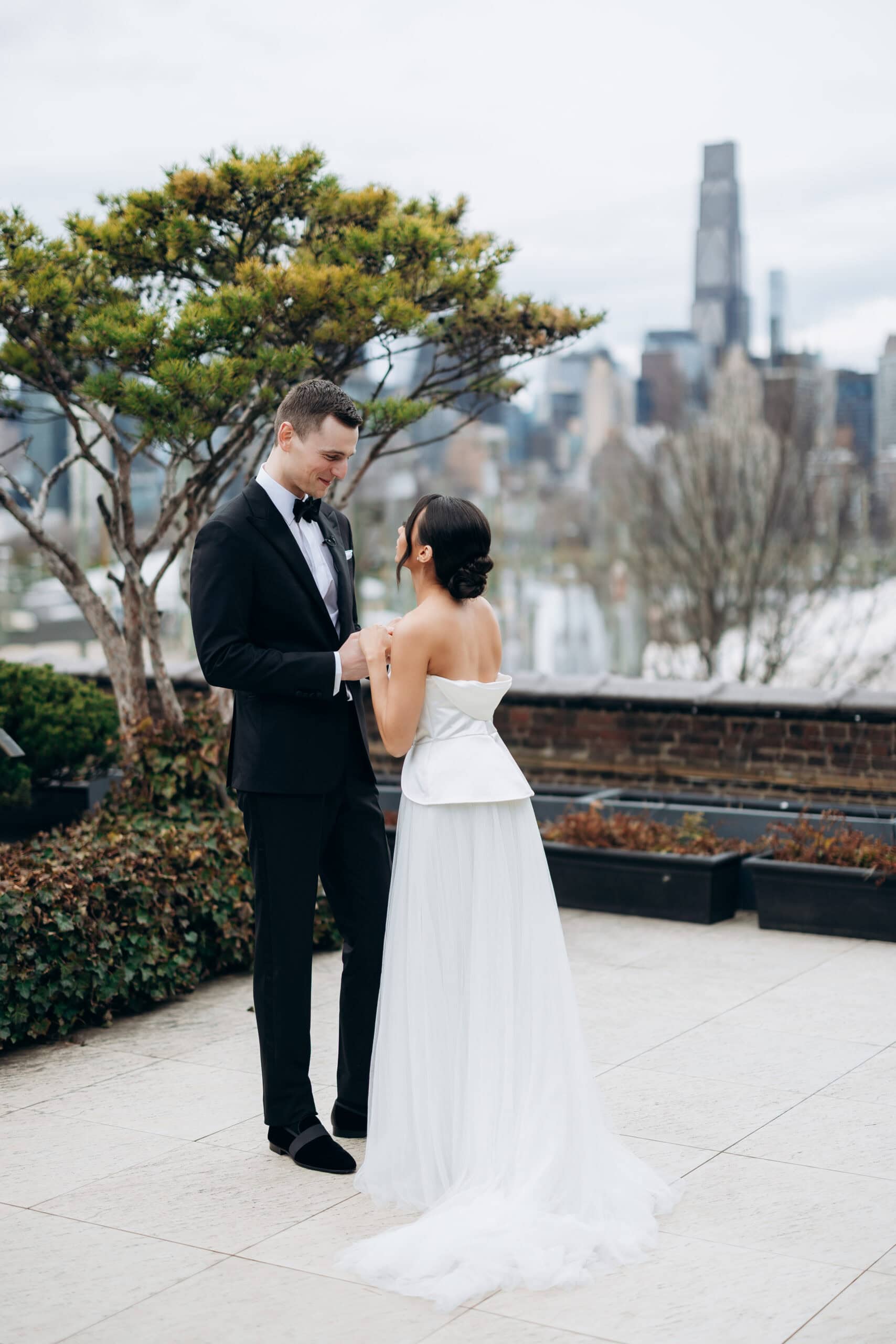 Bride and groom standing together on a rooftop terrace at The Foundry, with trees and the Manhattan skyline blurred behind them on an overcast day.