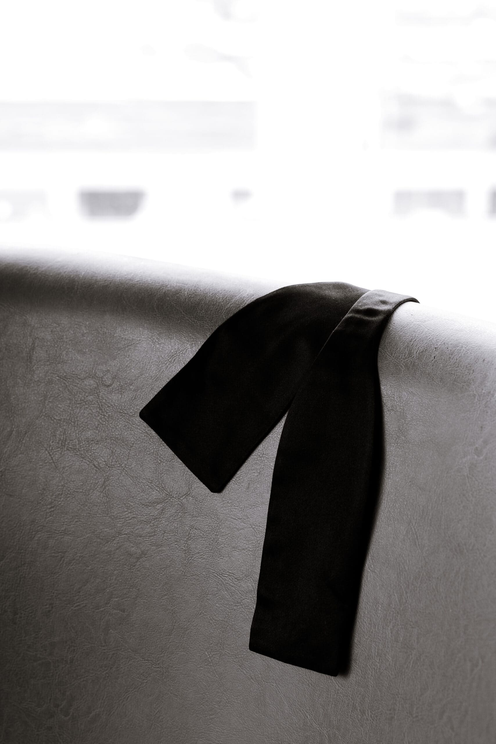 Close-up of a black satin ribbon draped over a pale leather seat near a bright window at The Foundry, photographed in soft natural light.