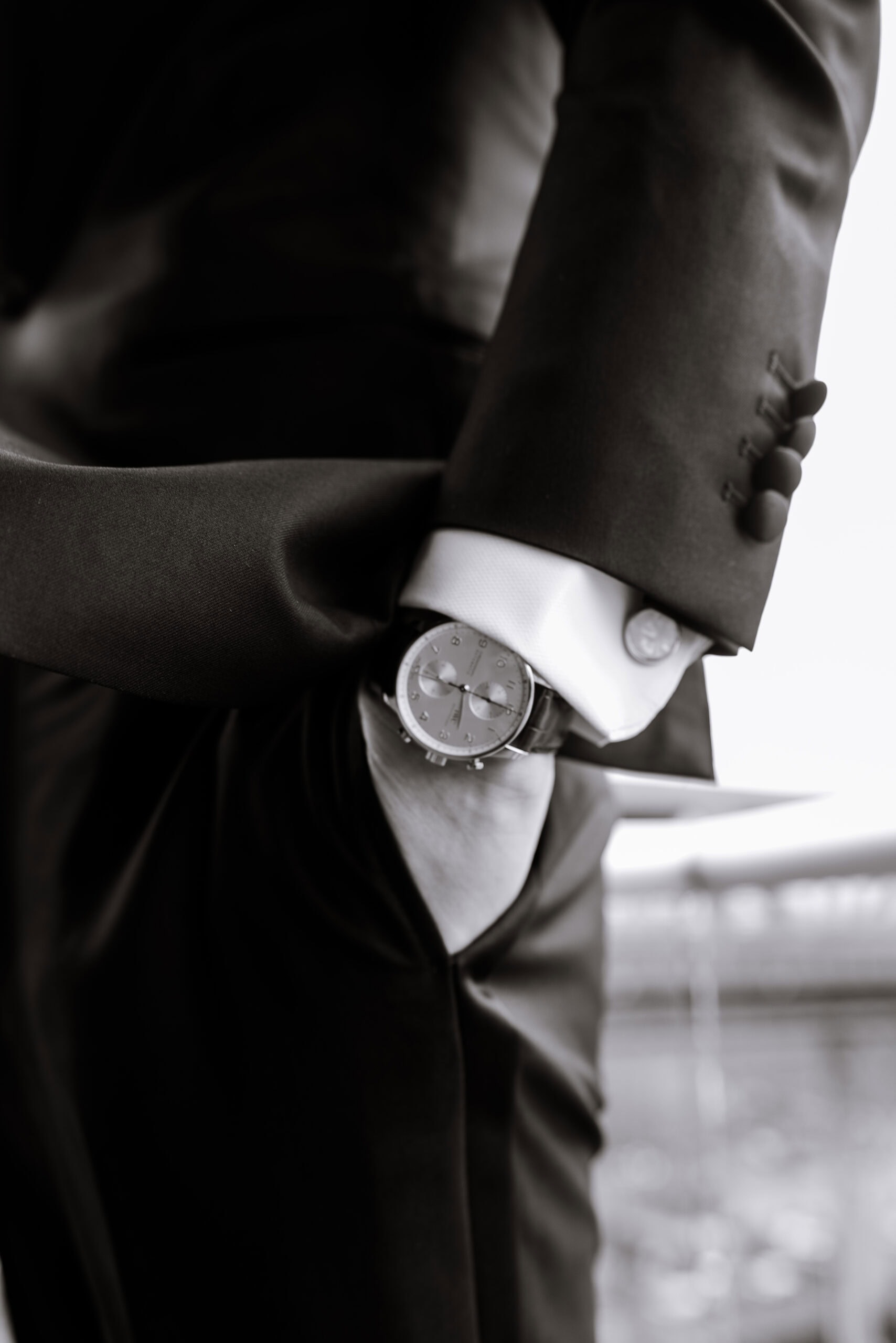 Close-up of a man in a black tuxedo adjusting his sleeve, showing a wristwatch and cufflink in soft window light at The Foundry.
