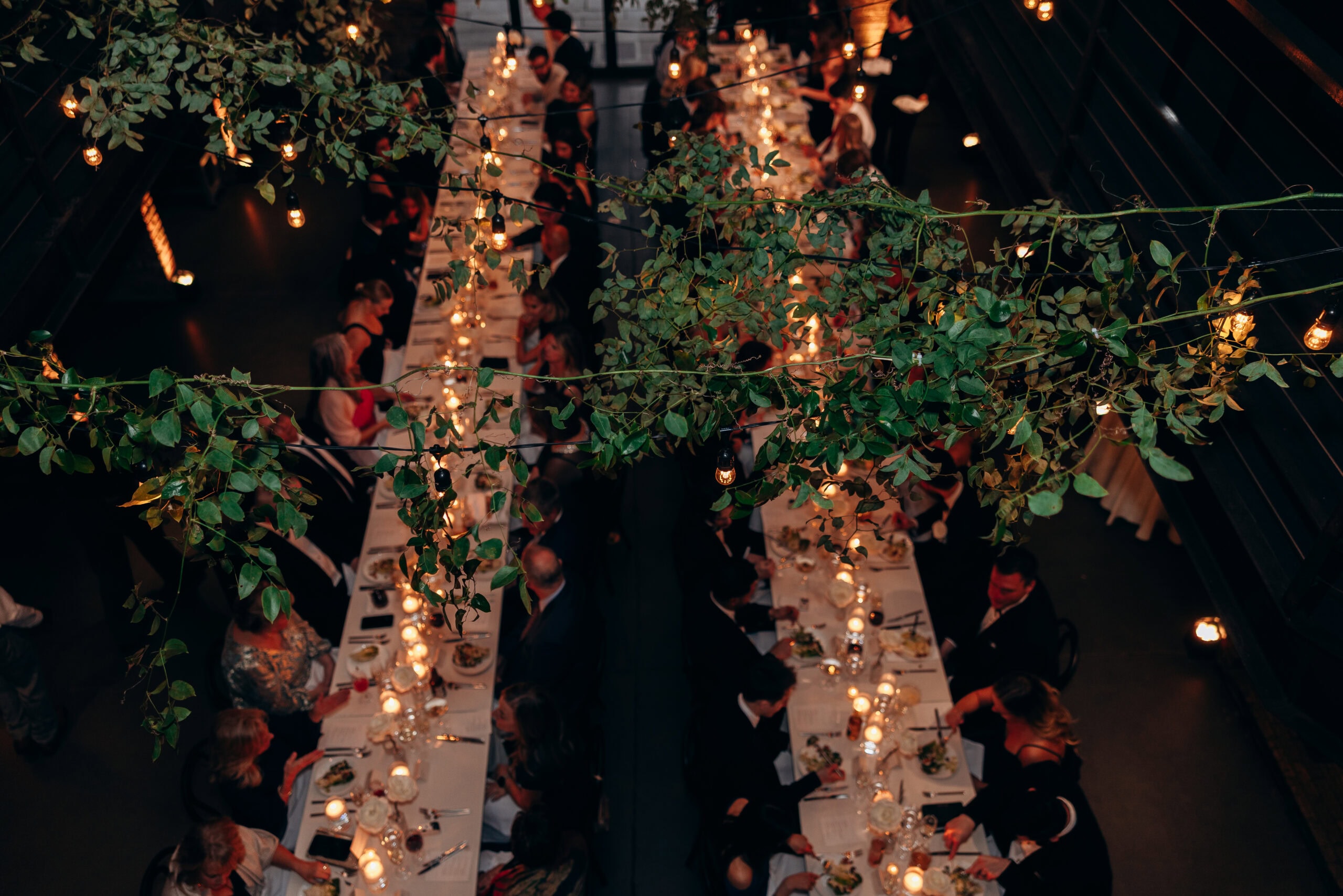 Overhead view of a wedding reception dinner at The Foundry, with long banquet tables, candles, string lights, hanging greenery, and seated guests.
