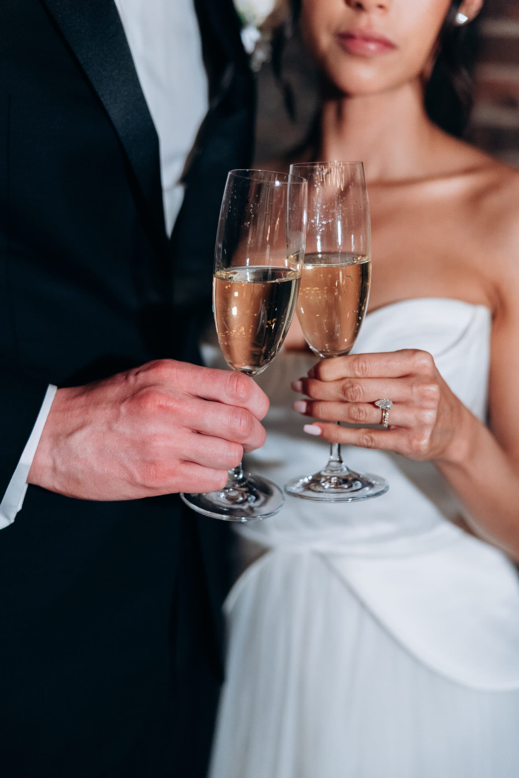 Close-up of a couple in wedding attire holding champagne flutes during a toast at The Foundry; a diamond engagement ring and strapless gown are in focus.