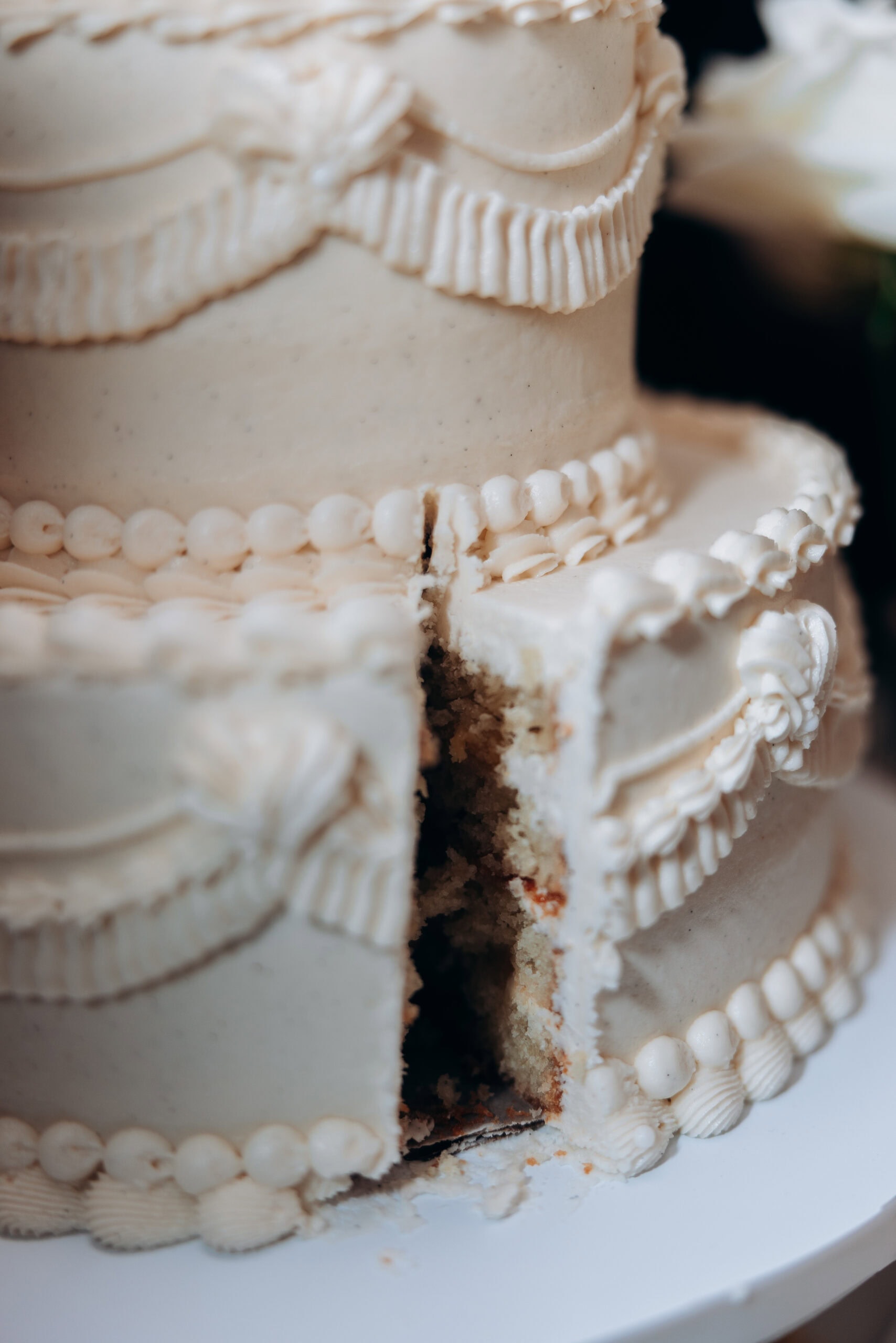 Close-up of a tiered ivory wedding cake at The Foundry with ornate piped frosting and a slice removed, revealing the interior crumb and filling.