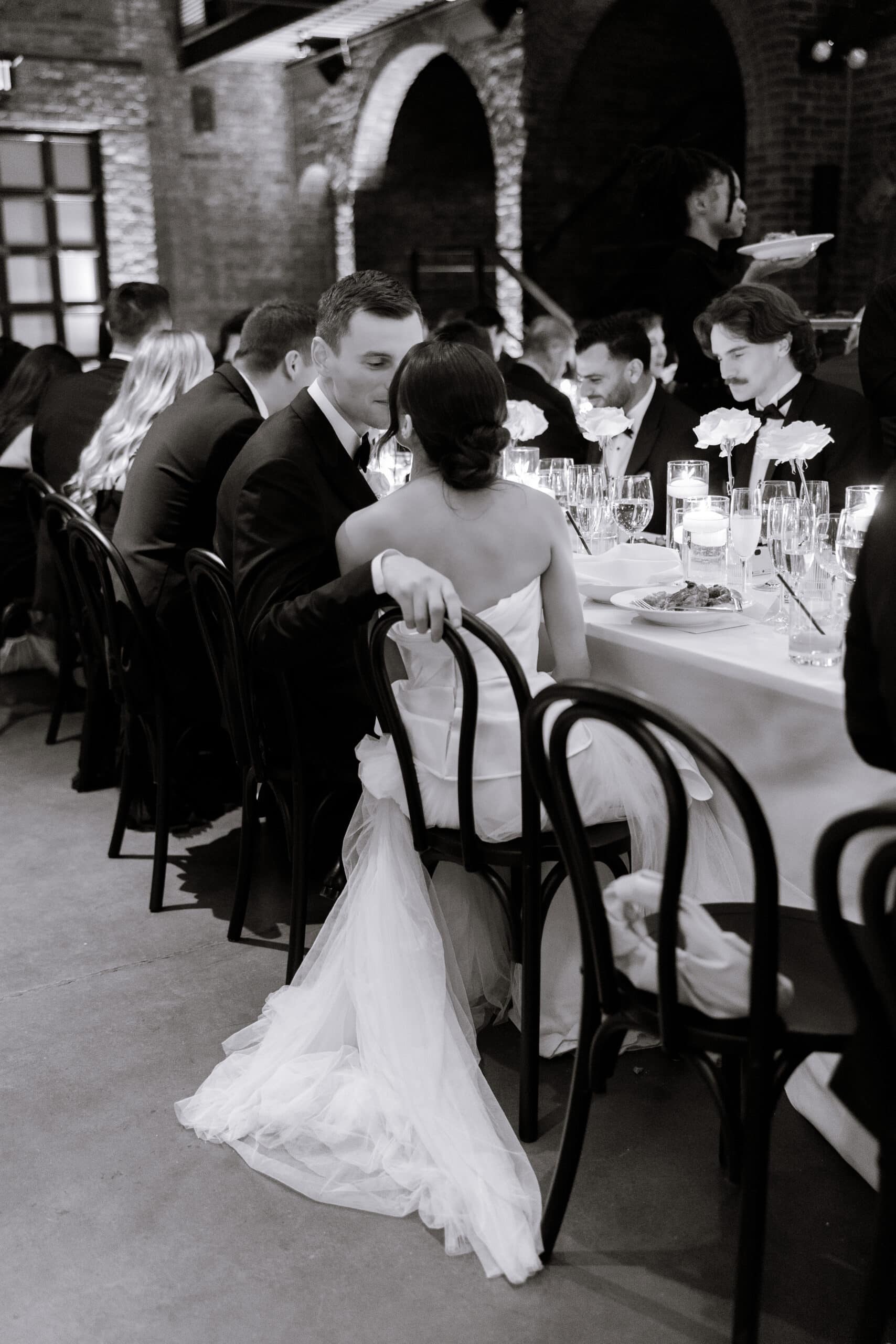 Black-and-white wedding reception at The Foundry, with the couple seated closely at a candlelit dinner table beneath brick arches.