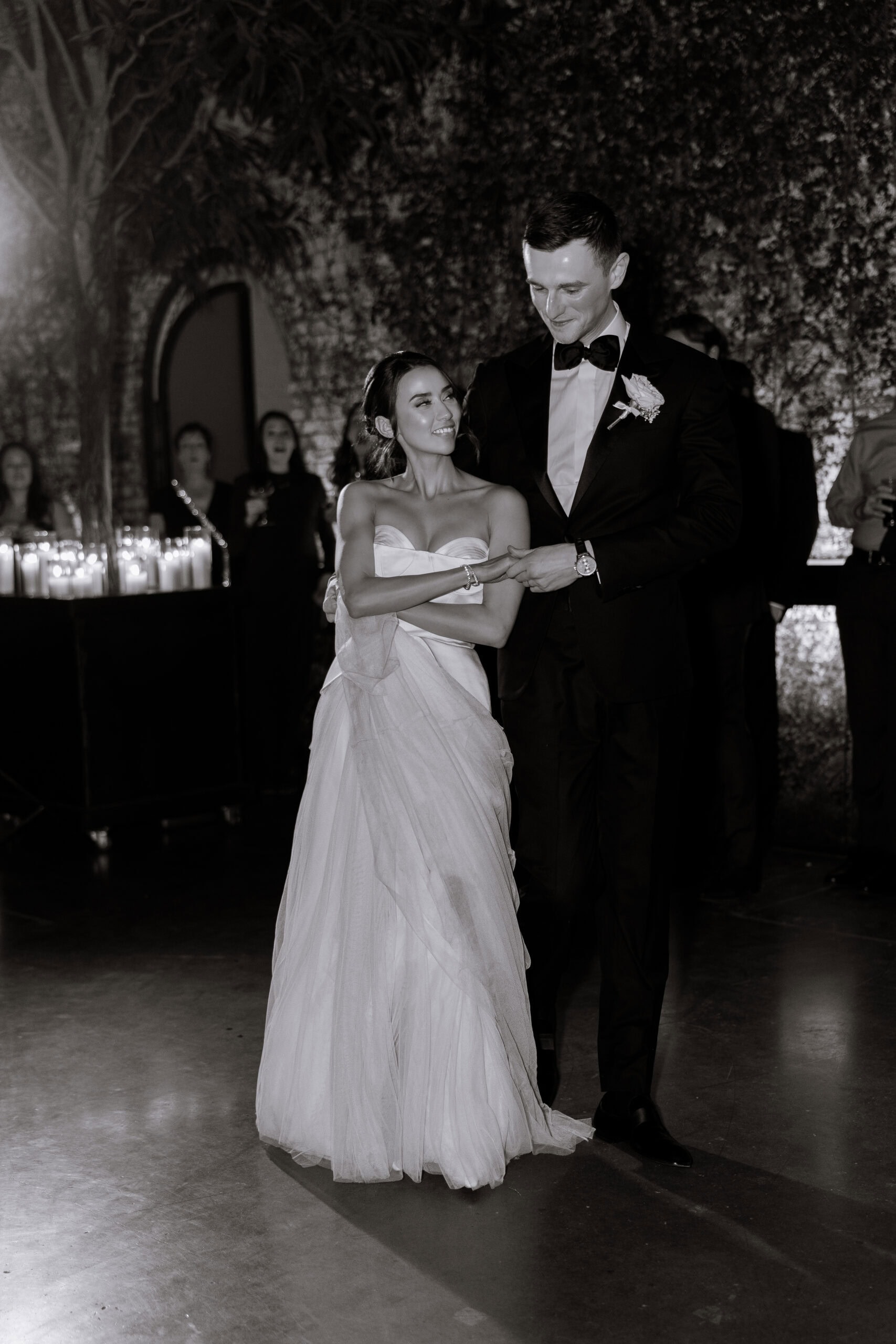 Black-and-white wedding reception photo of a couple sharing their first dance at The Foundry, surrounded by candlelight, guests, and an ivy-covered wall.