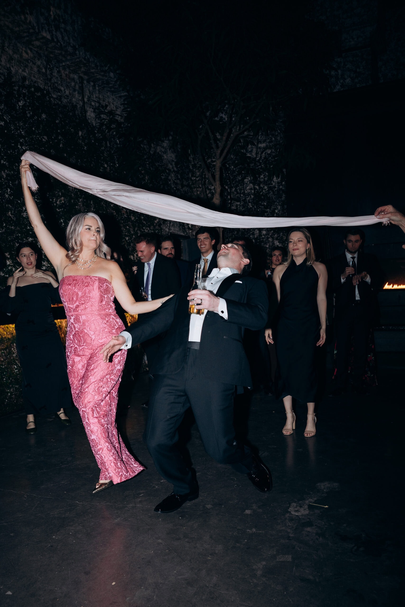 Guests play limbo on the dance floor at The Foundry during a nighttime wedding reception, with a woman in a pink strapless gown and a man in a tuxedo holding a beer.