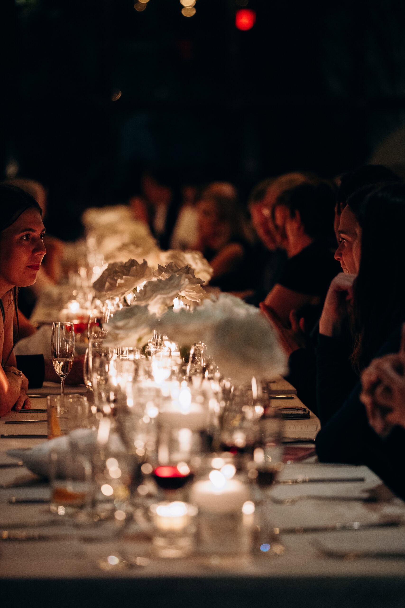 Guests seated along a long candlelit reception table at The Foundry, with white floral centerpieces, glassware, and a dark, intimate ambiance.