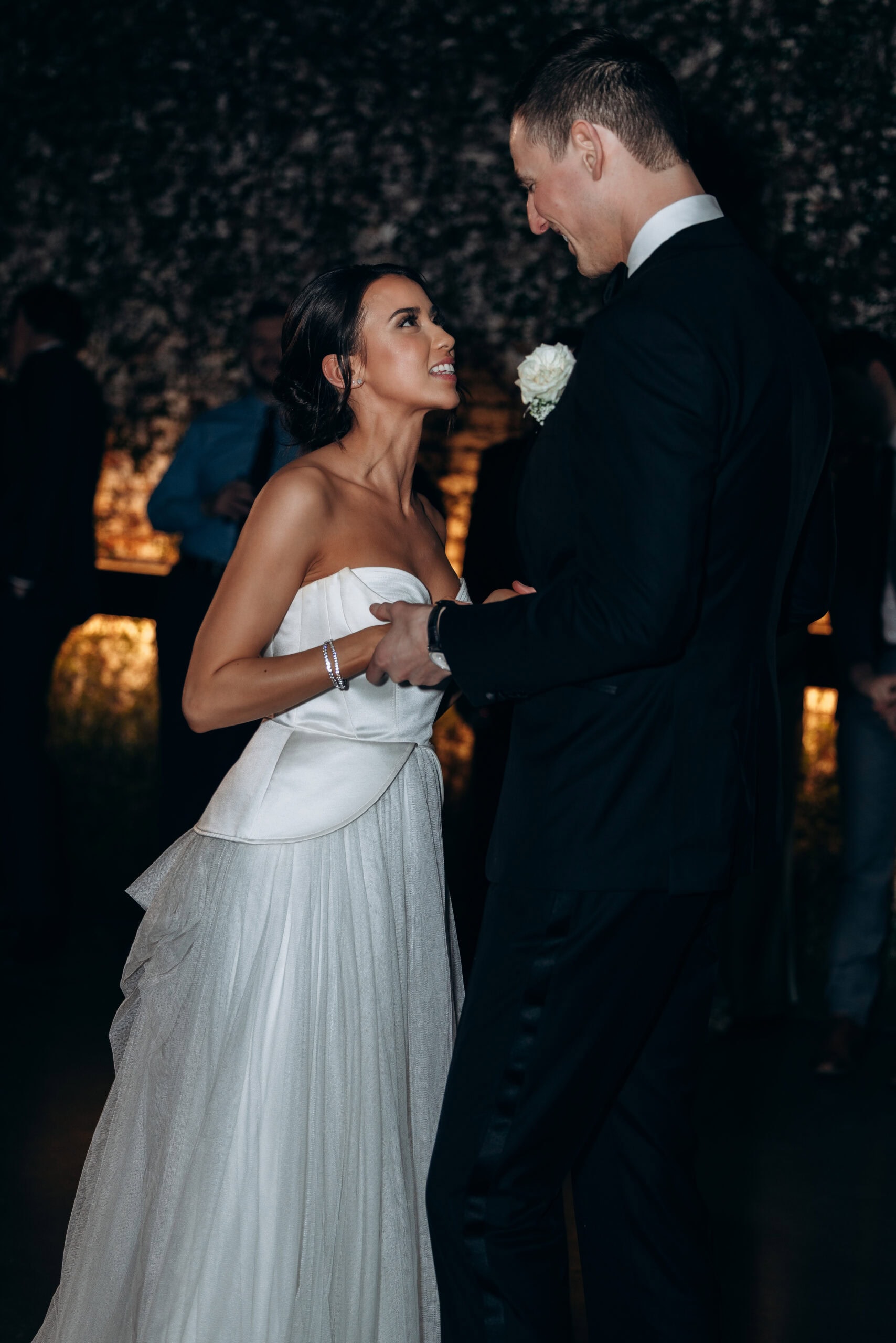 Bride in a strapless satin and tulle gown dances with groom in a black tuxedo during a dimly lit wedding reception at The Foundry.