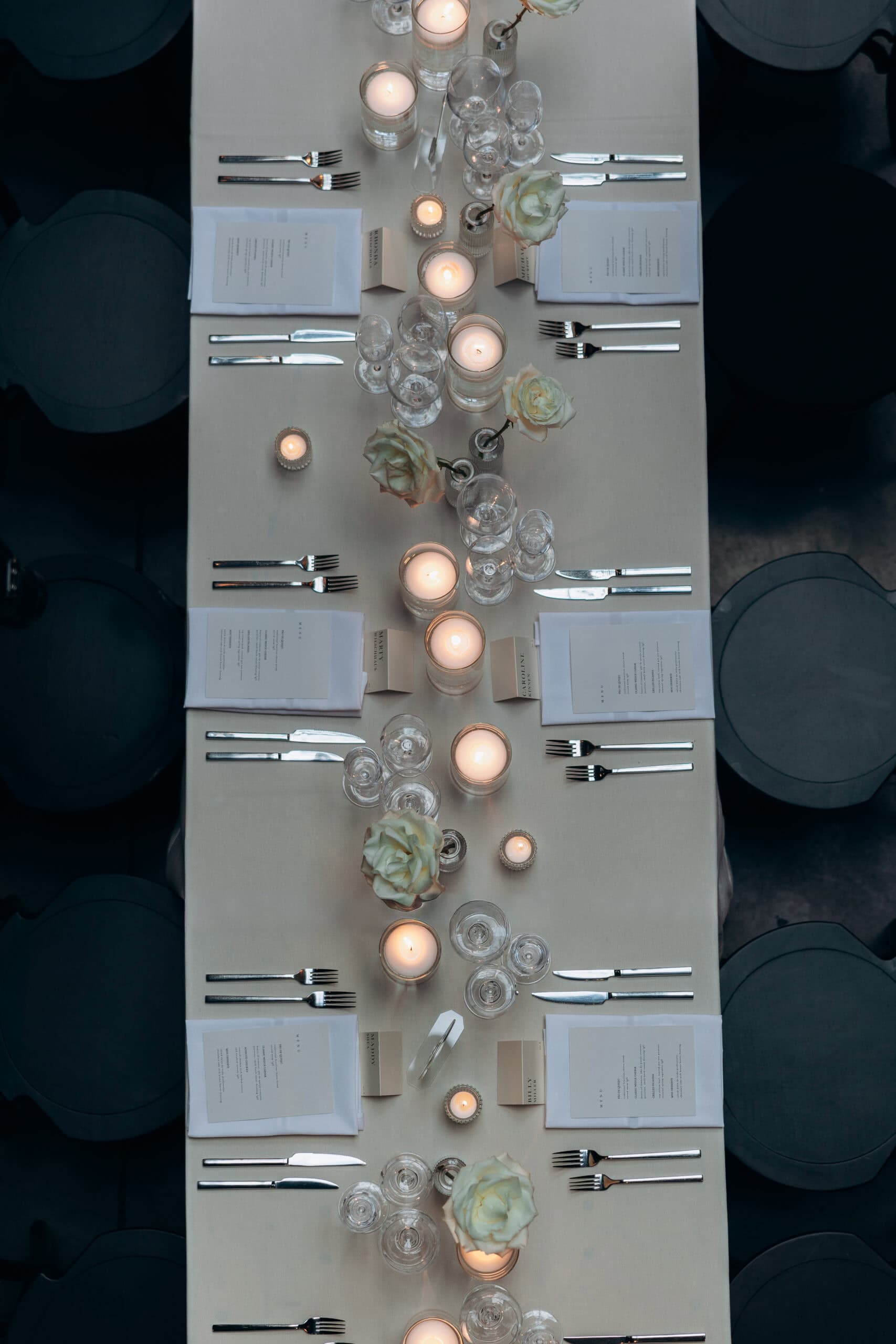 Overhead view of a long reception table at The Foundry with ivory linens, white roses, glowing candles, crystal glassware, menus, and silver flatware.