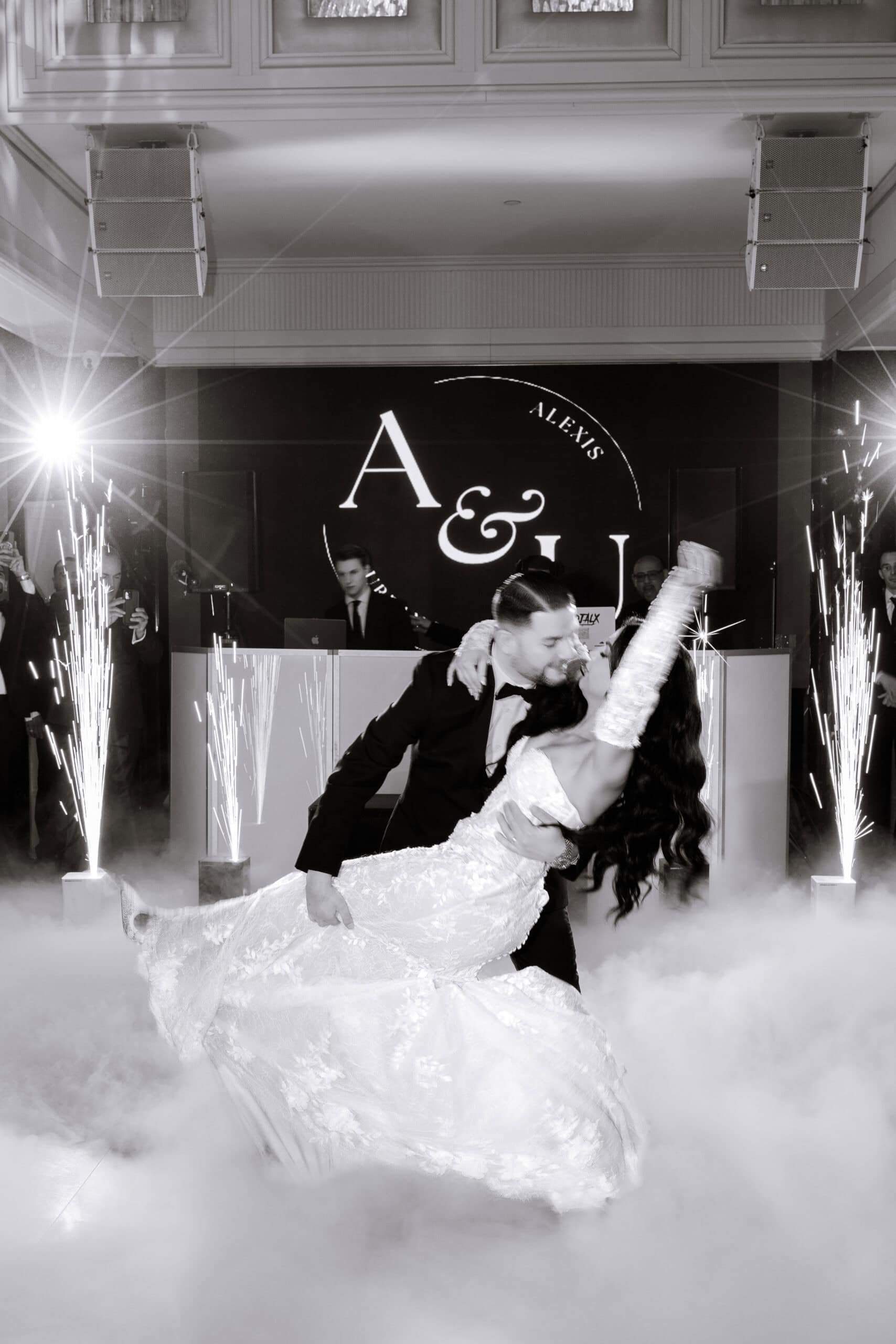 Bride and groom share a dramatic dip during their first dance surrounded by fog and sparklers, with guests and a DJ in the background at The Grand.