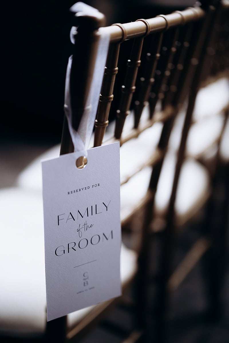 Close-up of a white reserved seating tag reading 'Family of the Groom' hanging from a gold Chiavari chair at a wedding venue.