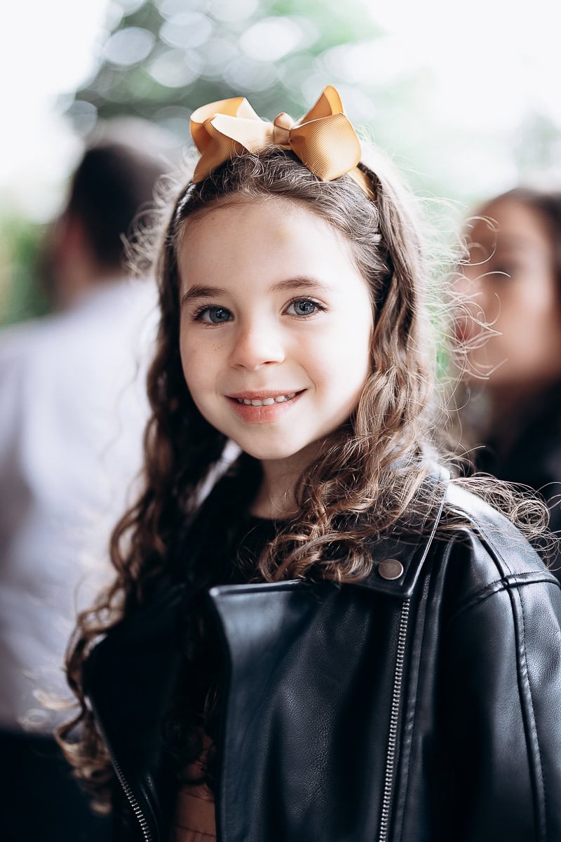Portrait of a young girl with curly hair wearing a black leather jacket and a gold ribbon headband, softly lit with blurred background at The Stone House, Warren, NJ.