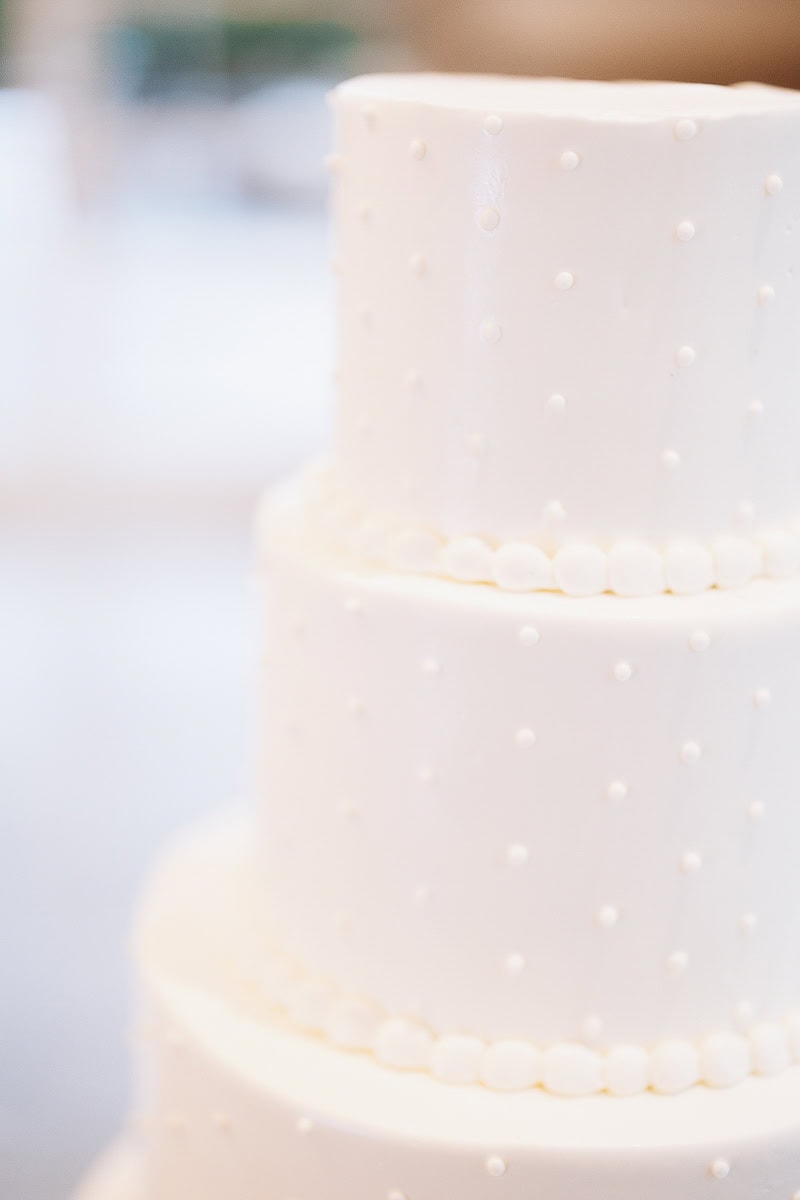 Close-up of a three-tier white wedding cake with textured buttercream dots and smooth pearl borders, soft natural light, The Stone House, Warren, NJ.