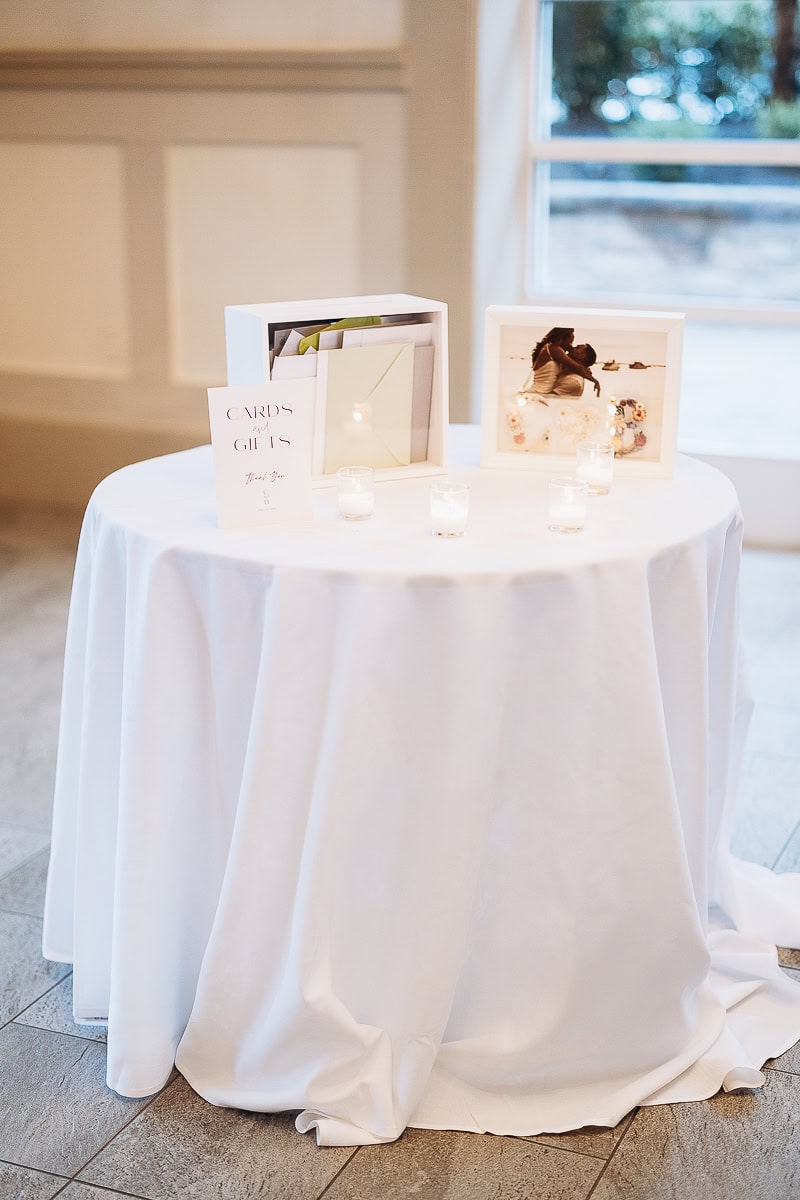 Round table draped in white linen with framed wedding photo, card box, and lit votive candles at The Stone House, Warren, NJ.