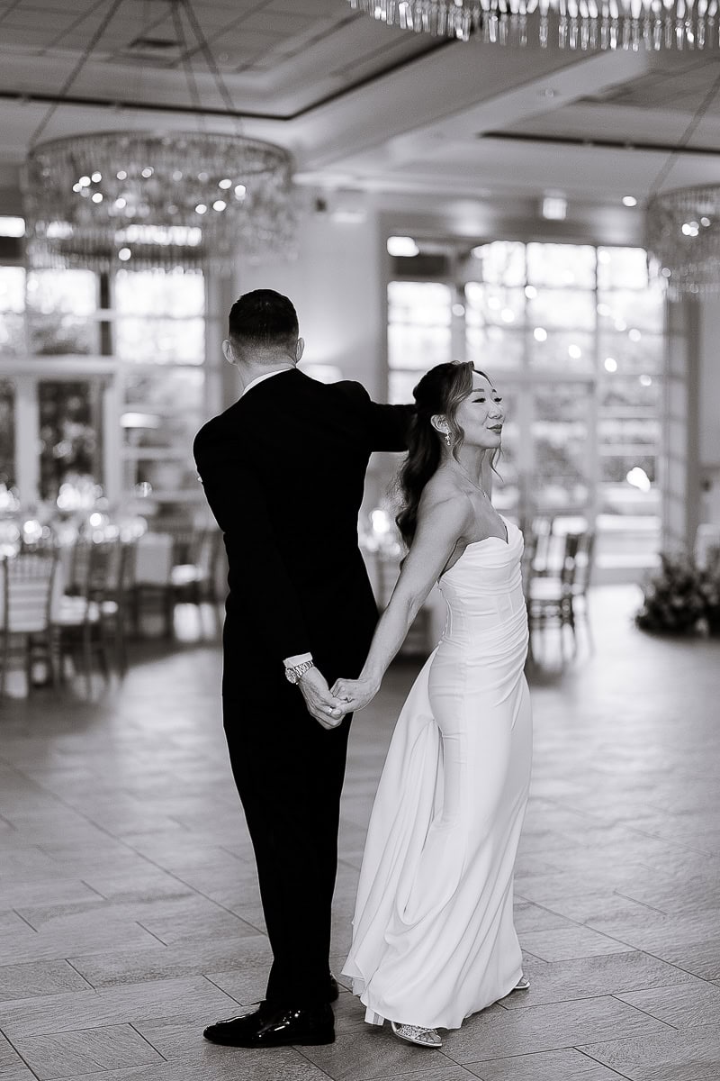 Bride and groom holding hands back-to-back in an elegant dance at The Stone House, Warren, NJ, with soft natural light and crystal chandeliers.
