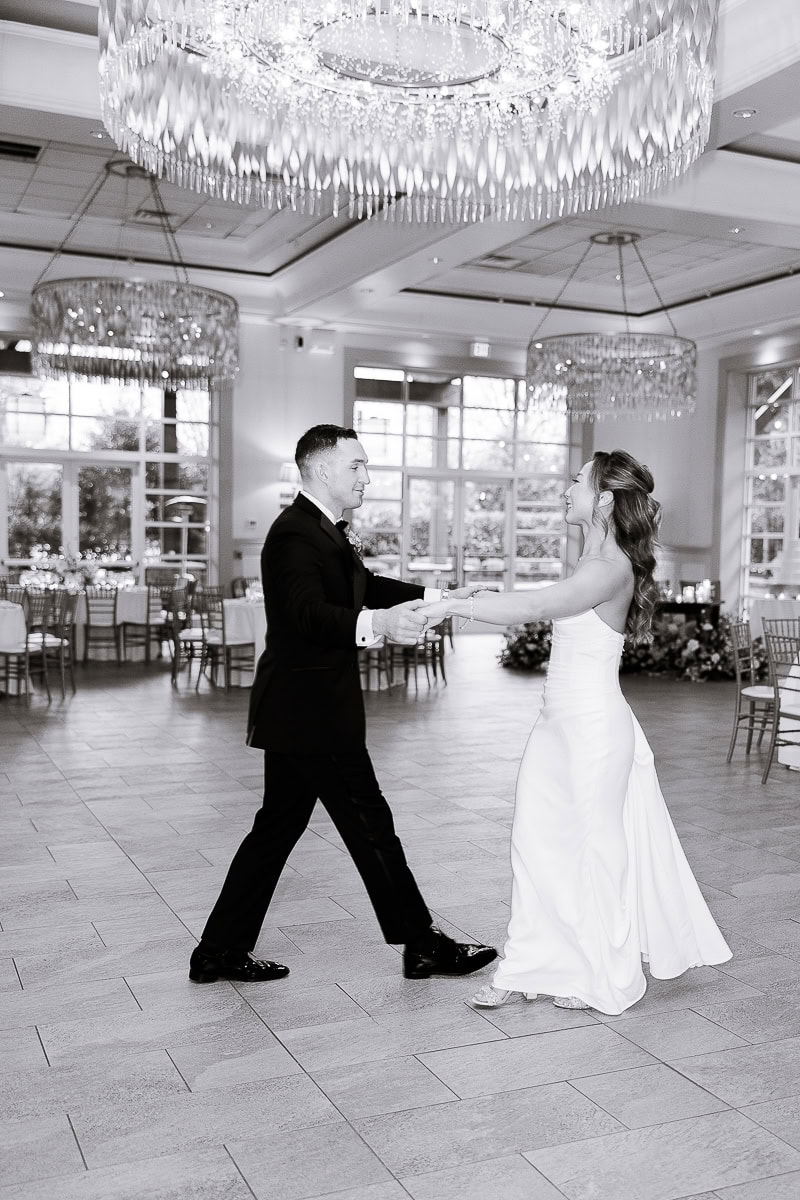 Bride and groom dancing in an elegant reception hall with large crystal chandeliers and tiled floor at The Stone House, Warren, NJ.