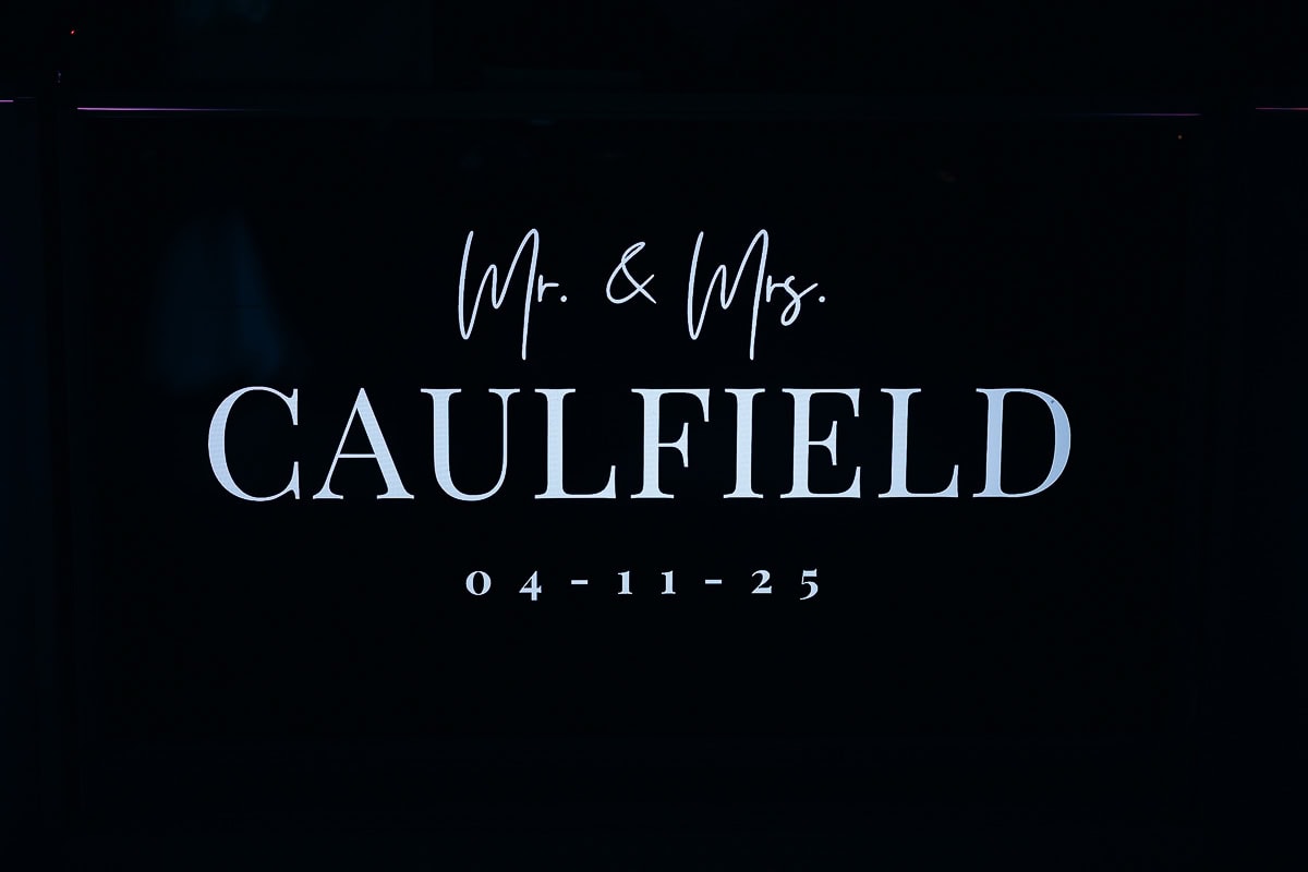 Illuminated wedding monogram sign reading 'Mr. & Mrs. Caulfield' with date 04-11-25 in elegant white typography on black background.