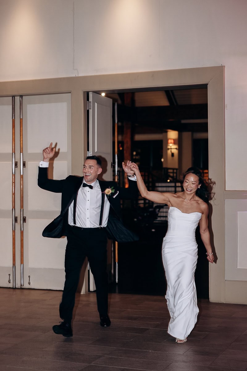 Bride and groom holding hands, entering a room with joyful expressions and lively movement at The Stone House, Warren, NJ.
