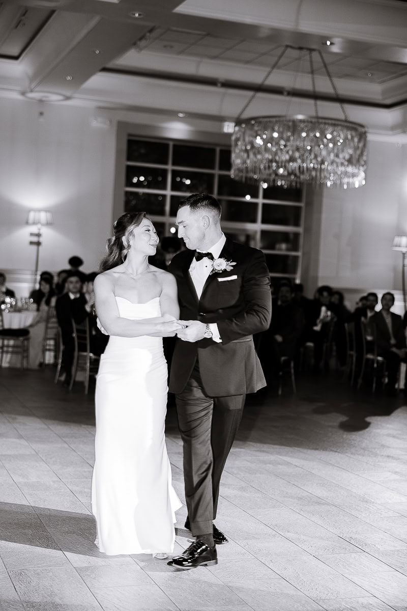 Bride and groom share an intimate first dance in a softly lit ballroom with a crystal chandelier, surrounded by seated guests at The Stone House, Warren, NJ.