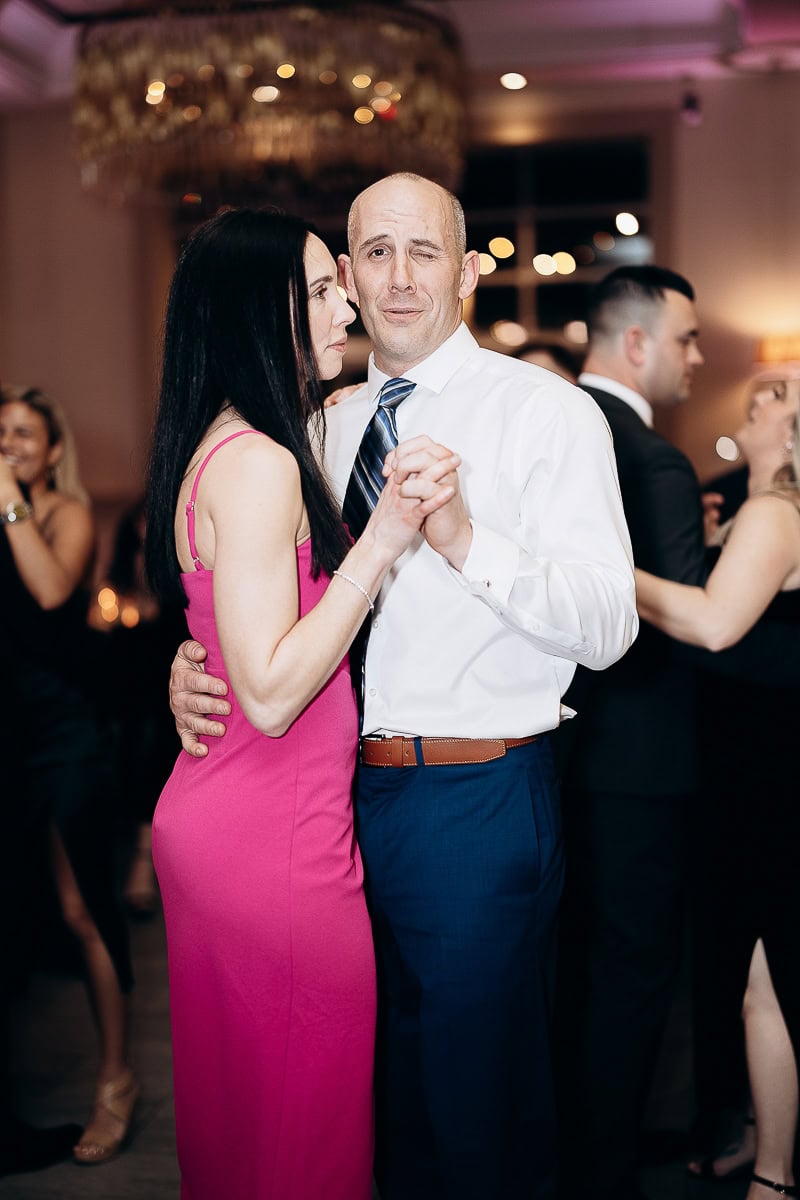 Man and woman dancing closely at a wedding reception, with chandelier lights softly glowing in the background.