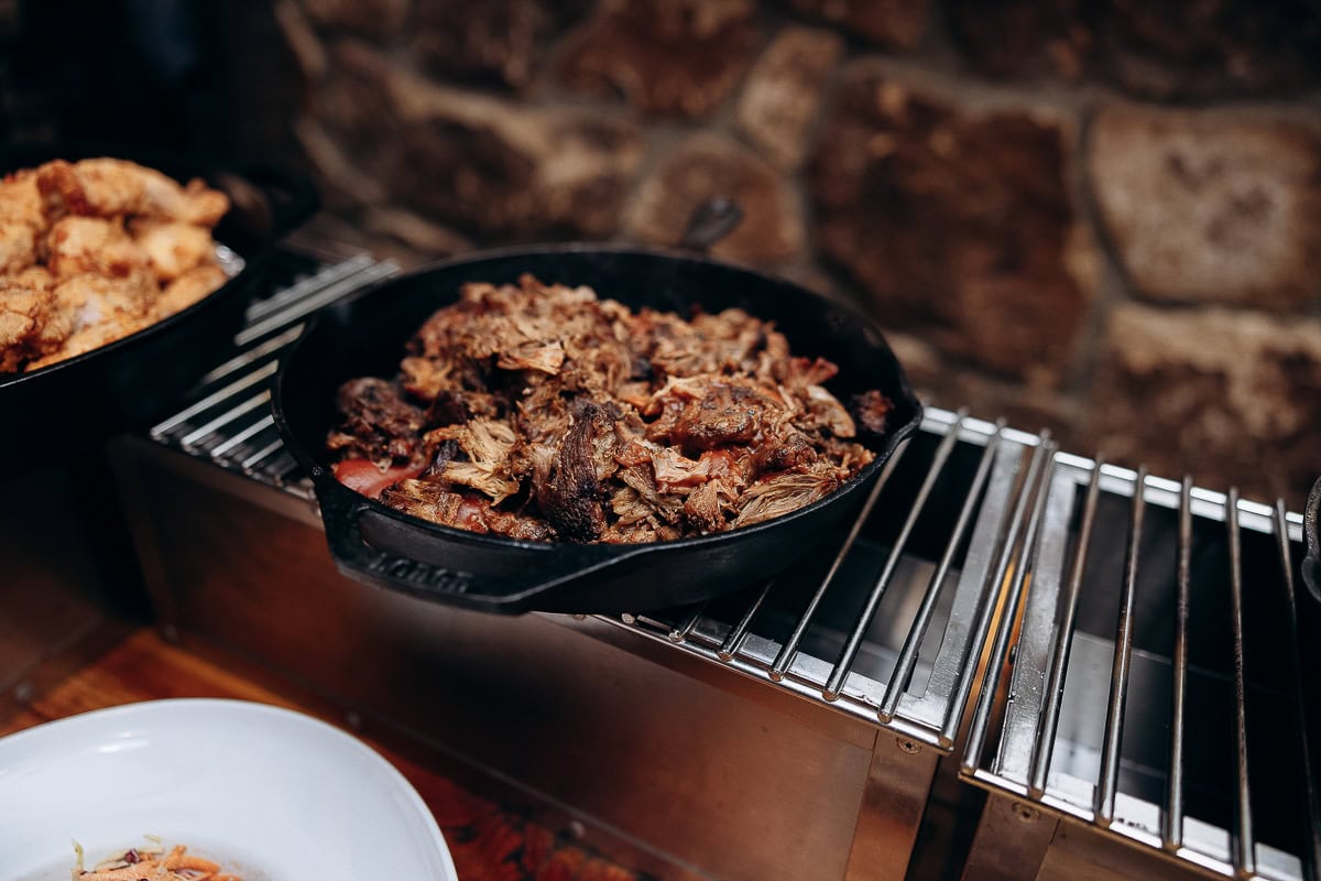 Cast iron skillet filled with braised meat on a warming rack with stone wall background at The Stone House, Warren, NJ.