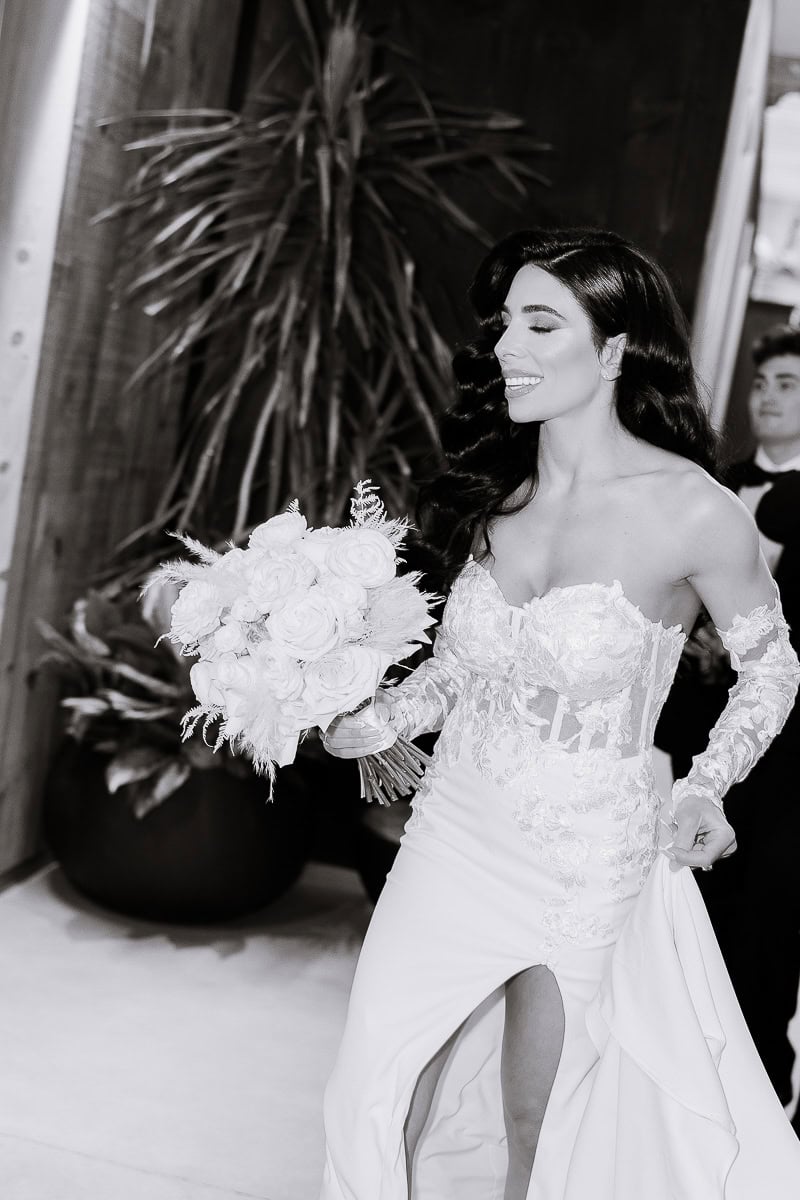 B&W bride in lace corset gown with white rose bouquet, walking indoors at The Switch House by Cescaphe, Philadelphia.