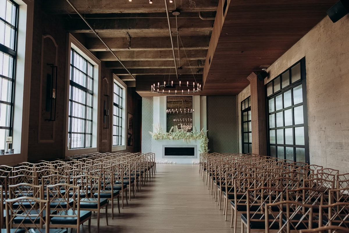 Empty ceremony setup with rattan chairs, floral fireplace, ring chandeliers, and industrial windows at The Switch House, Philadelphia.