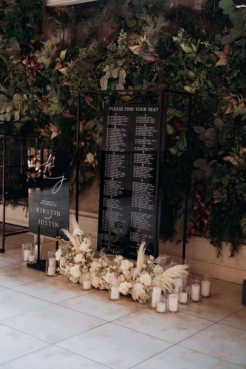 Wedding seating chart and welcome sign with white florals and candles before a greenery wall at The Switch House by Cescaphe, Philadelphia.