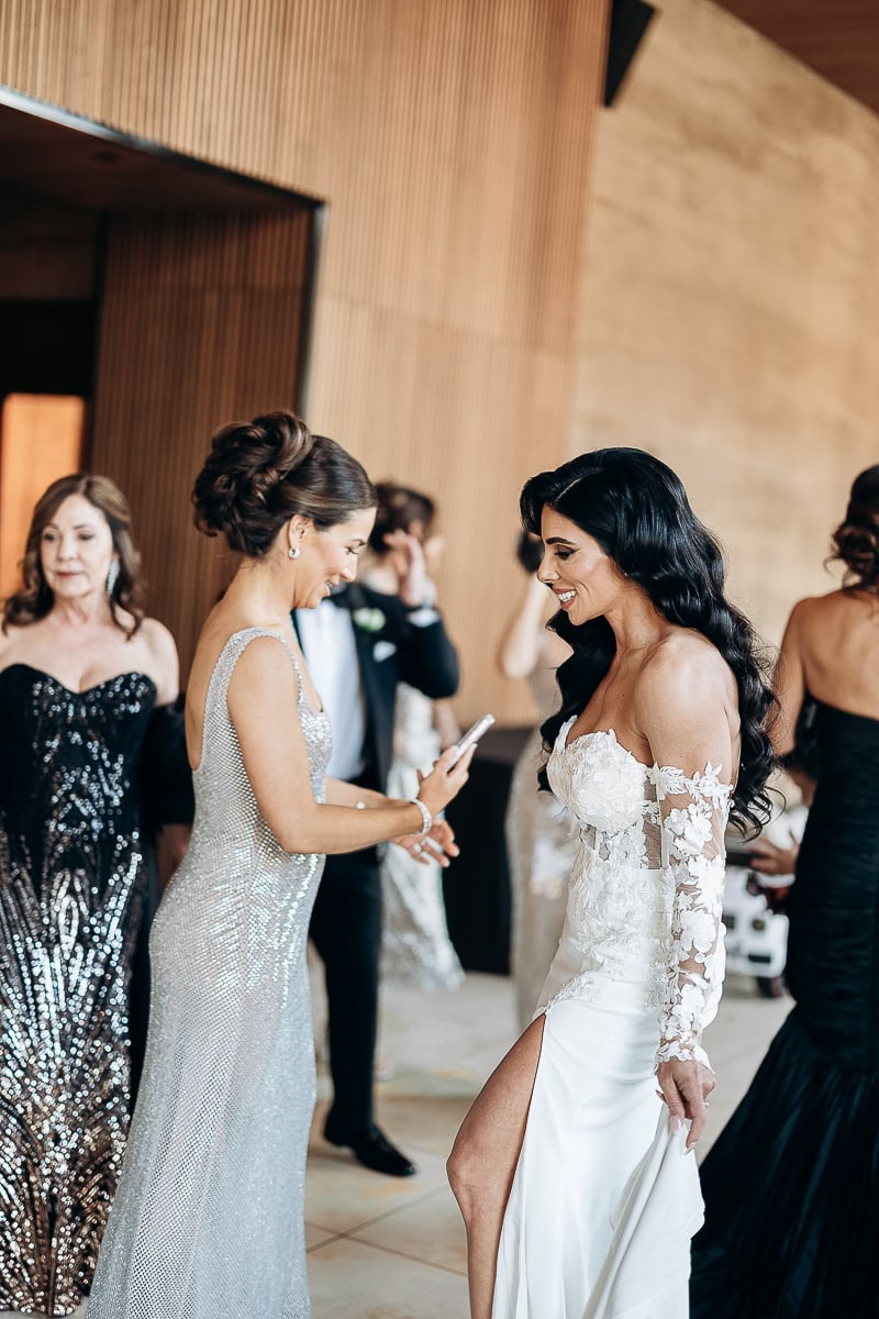 Bride in off-shoulder lace gown smiling with guest in silver dress inside The Switch House, Philadelphia.