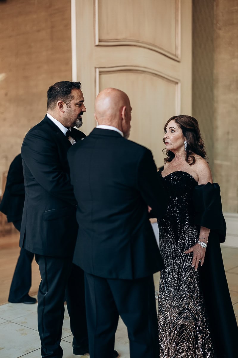 Three guests in black-tie converse indoors; sequined gown and tuxedos under soft light at The Switch House by Cescaphe, Philadelphia.