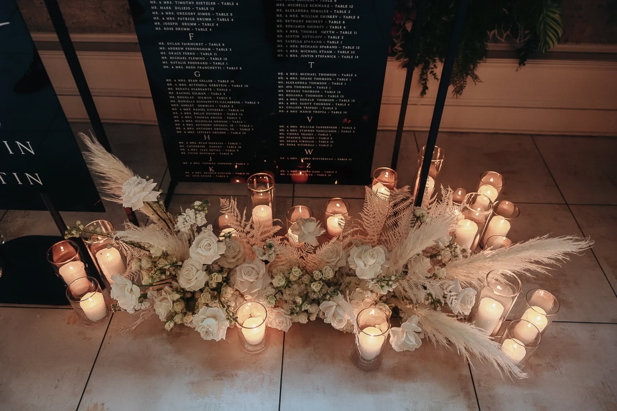 Glass candles encircle ivory roses, lisianthus, and pampas beneath black seating charts at The Switch House by Cescaphe, Philadelphia.