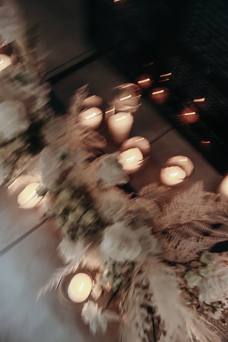 Soft-focus votive and pillar candles among white roses and bleached ferns along an aisle at The Switch House by Cescaphe, Philadelphia.